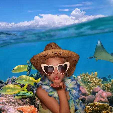 Child wearing heart-shaped sunglasses, blowing a kiss underwater with fish and coral in a snorkeling scene.
