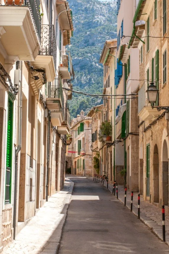 Smal sydlandsk gade med farverige bygninger og udsigt til bjergene – symbol på overblik i kvalitet, selv når systemet virker snævert.