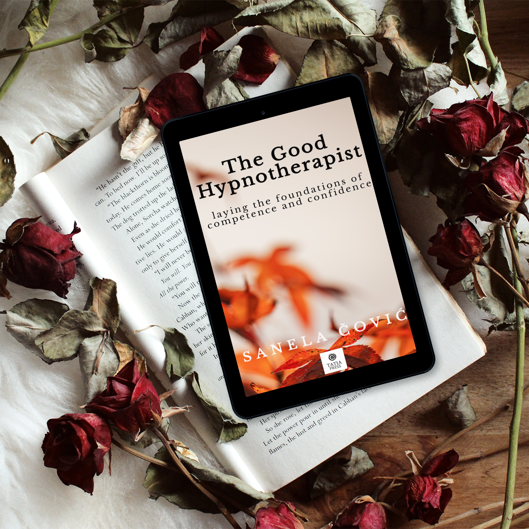 A tablet displaying a book cover titled "The Good Hypnotherapist" by Sanela Covic, surrounded by dried roses and an open book on a wooden surface.