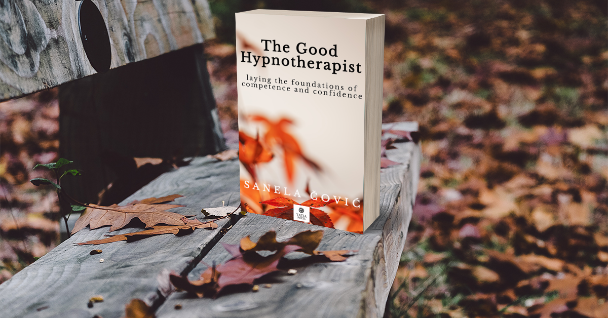 A book titled 'The Good Hypnotherapist' by Sanela Ćović standing on a weathered wooden park bench covered with fallen autumn leaves
