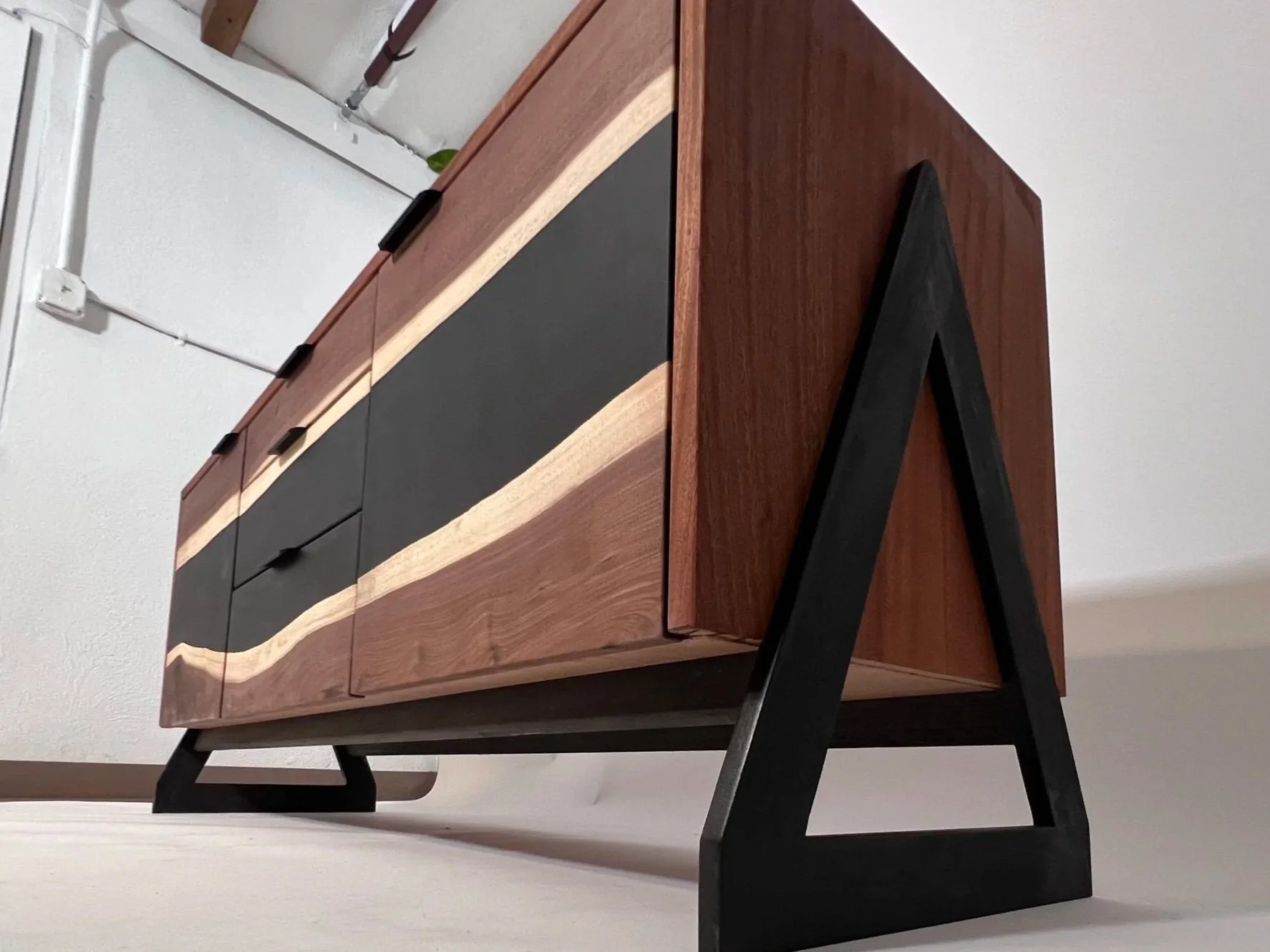Wooden sideboard with black and natural wood accents on a white surface, against a white wall with electrical outlets.