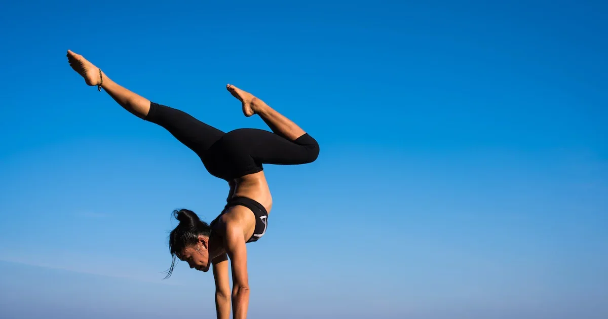 Woman practicing advanced yoga handstand outdoors—perfect balance, flexibility, and core control under a clear blue sky.