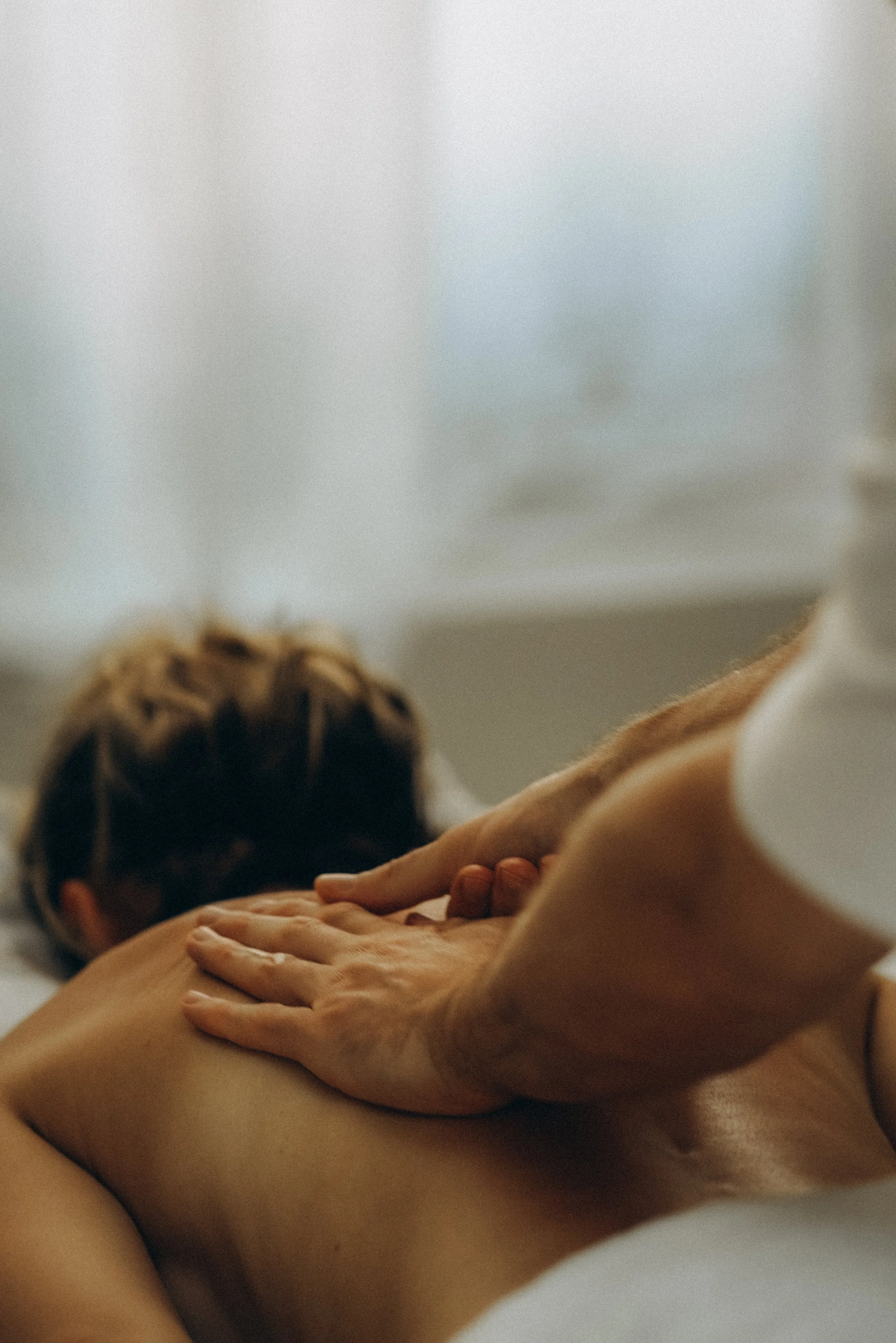 A person receiving a massage, lying face down on a massage table with a blanket over their lower back, while a masseuse's hands press into the person's back.