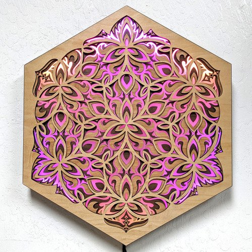 Decorative wooden wall art with intricate laser-cut floral and geometric patterns, illuminated with purple and pink lighting, mounted on a white wall.