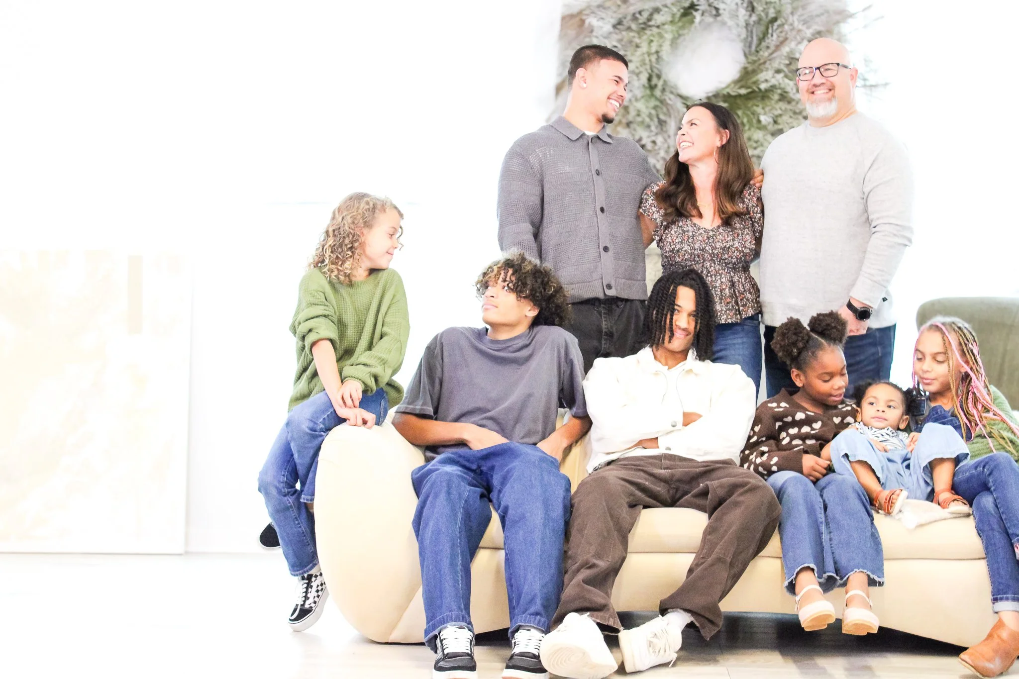 A diverse family photo with adults and children smiling and sitting on a couch in a bright living room.