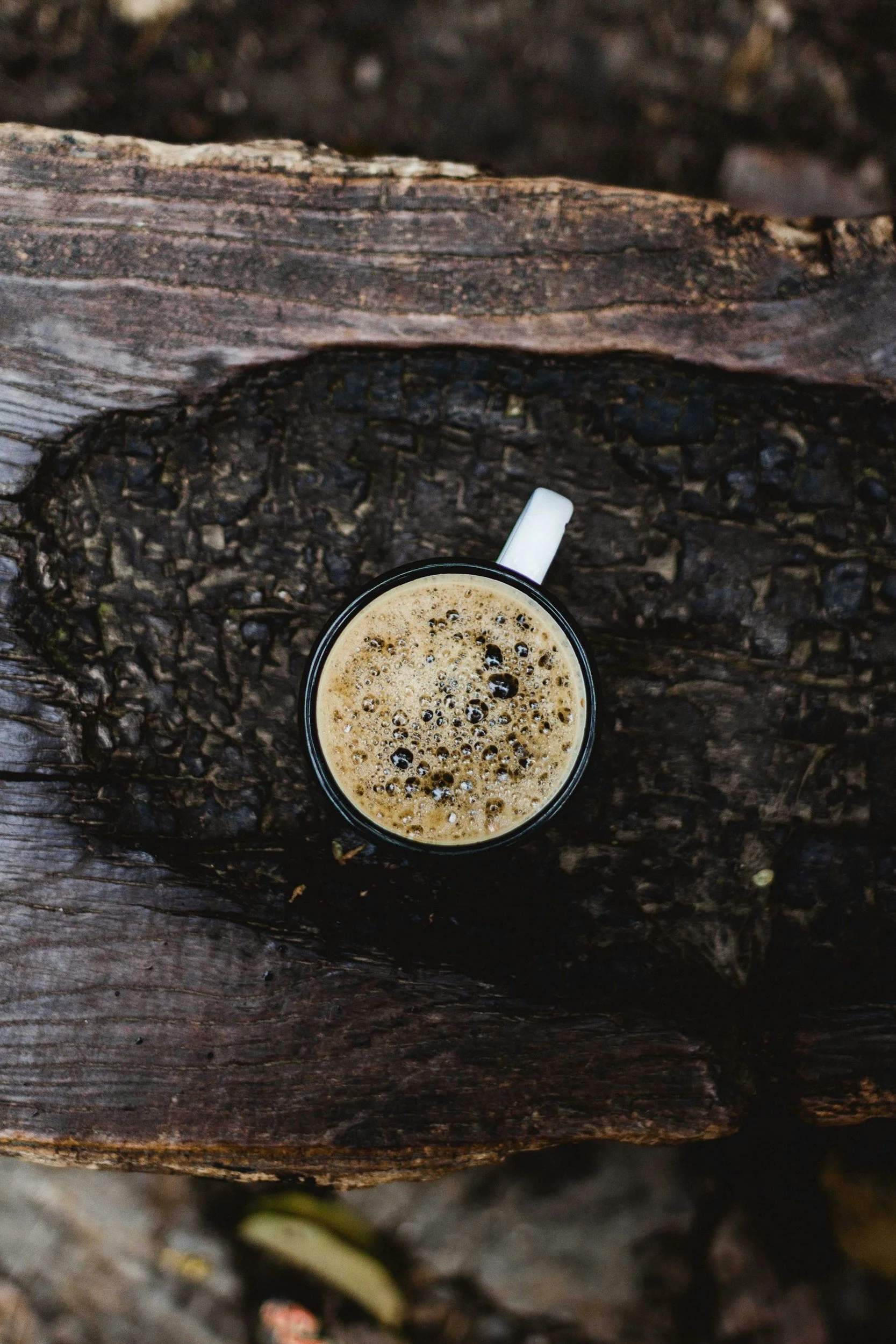 Top-down view of a mug of hot coffee with foam on a weathered wooden surface.