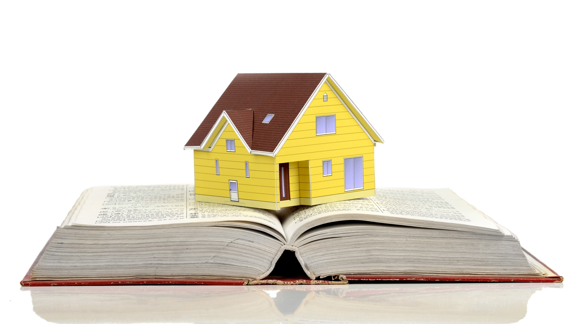 A yellow model house with brown roof sitting on an open book, symbolizing real estate or homeownership.