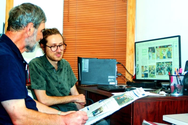 Two volunteers work on desktop publishing at a computer.