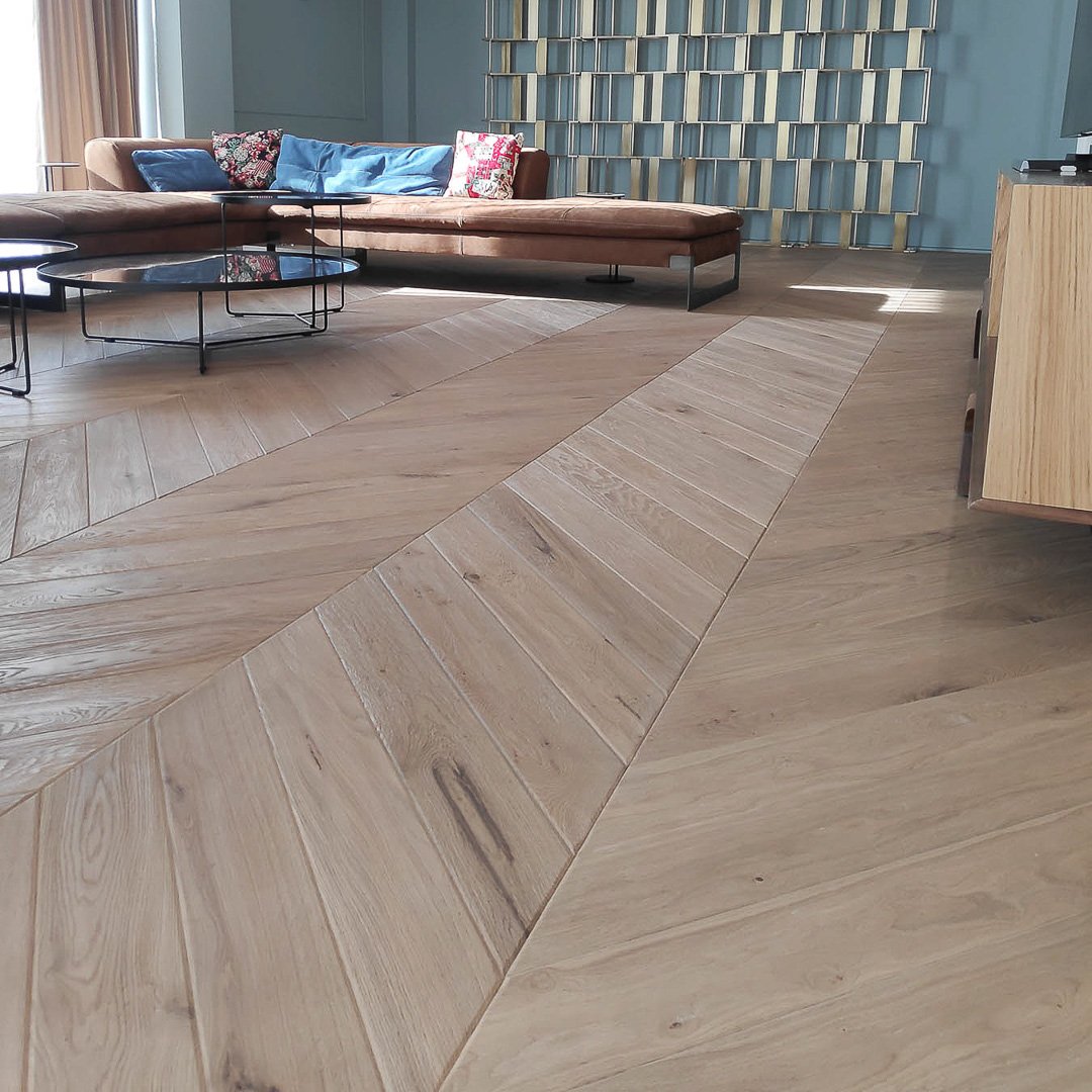 Sala moderna con piso de madera de patrón diagonal y mueble de sofá marrón con cojines azules, en una sala bien iluminada con paredes azules y decoración moderna.