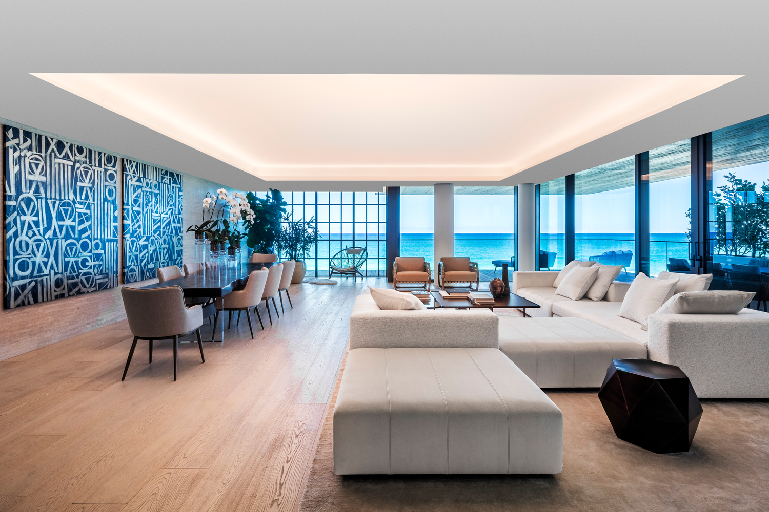 Sala de estar moderna con vista al mar, sillones beige, mesa de centro, decoración con plantas y arte en la pared