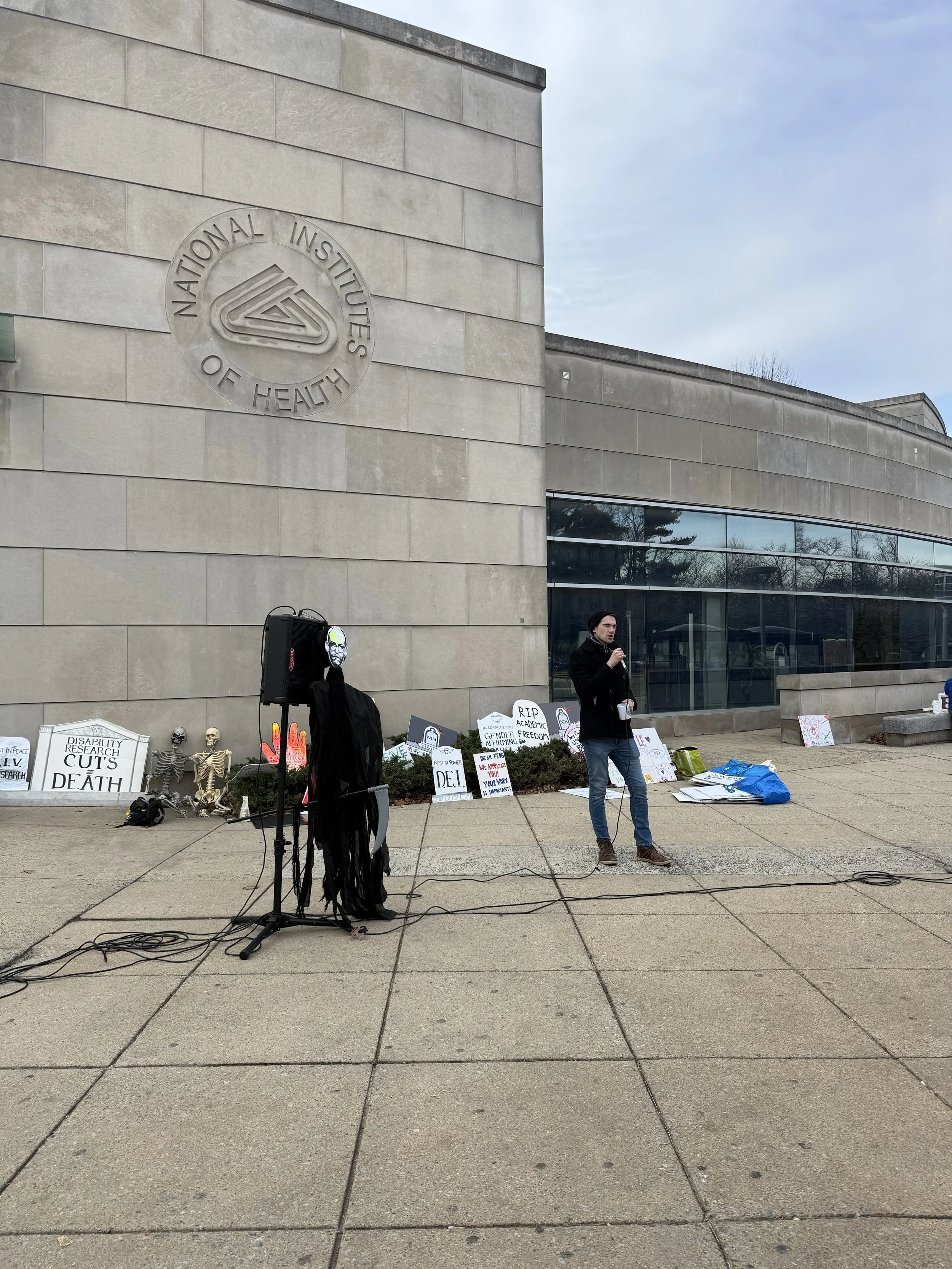 A person speaks into a microphone at an NIH vigil