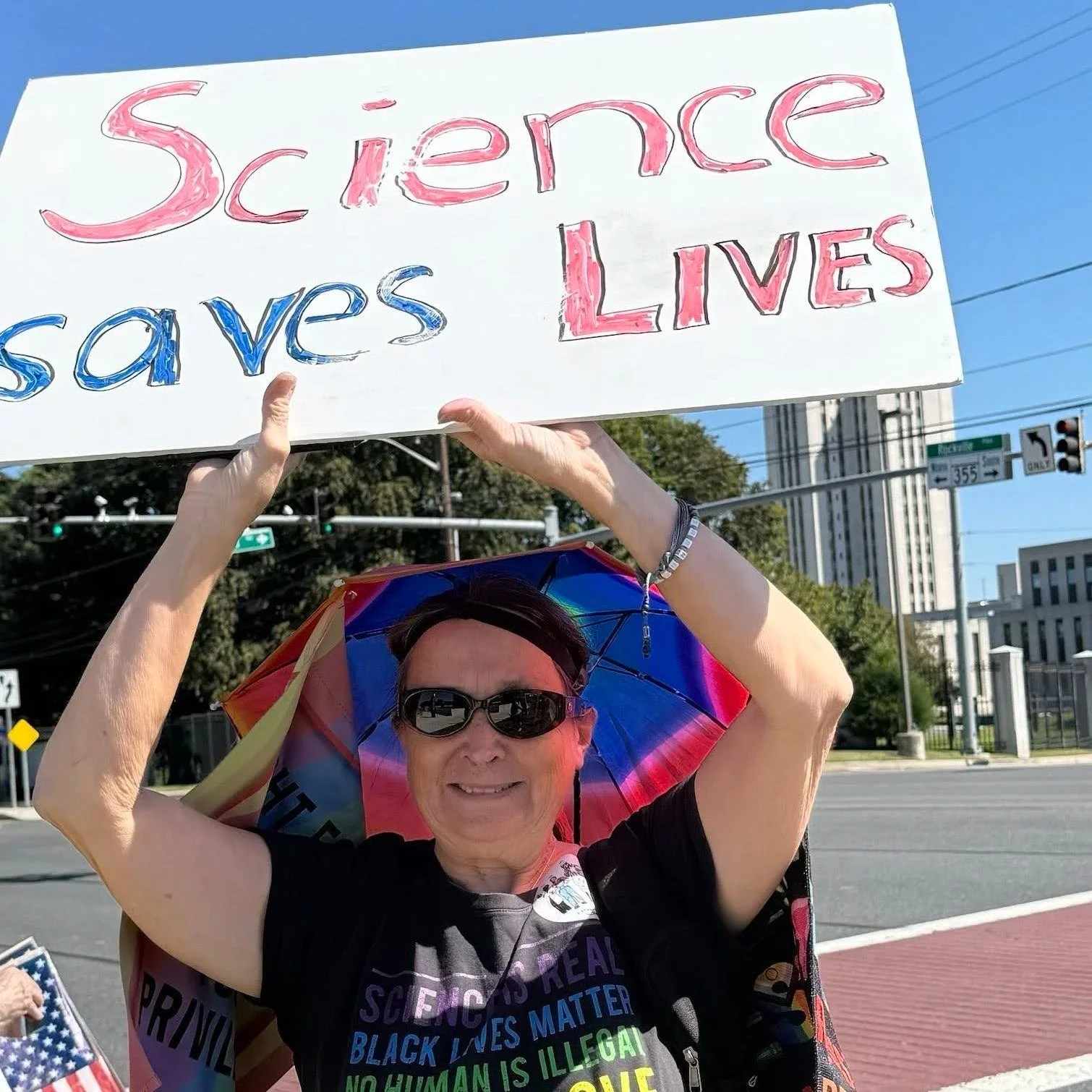 A woman wearing sunglasses and holding a Science Saves Lives sign.
