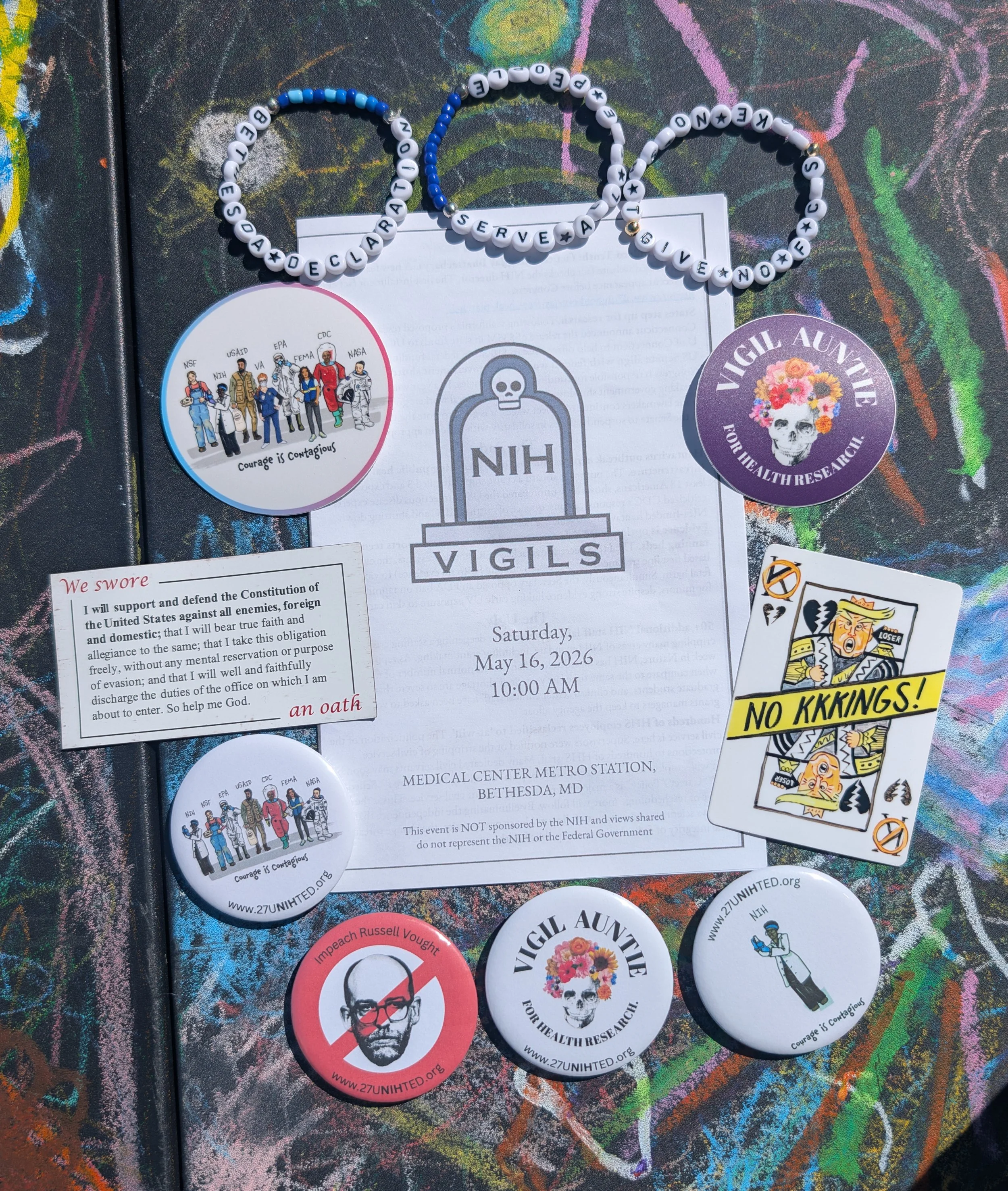 A colorful merch table with a vigil program and various pins, stickers, cards, and bracelets with vigil messaging