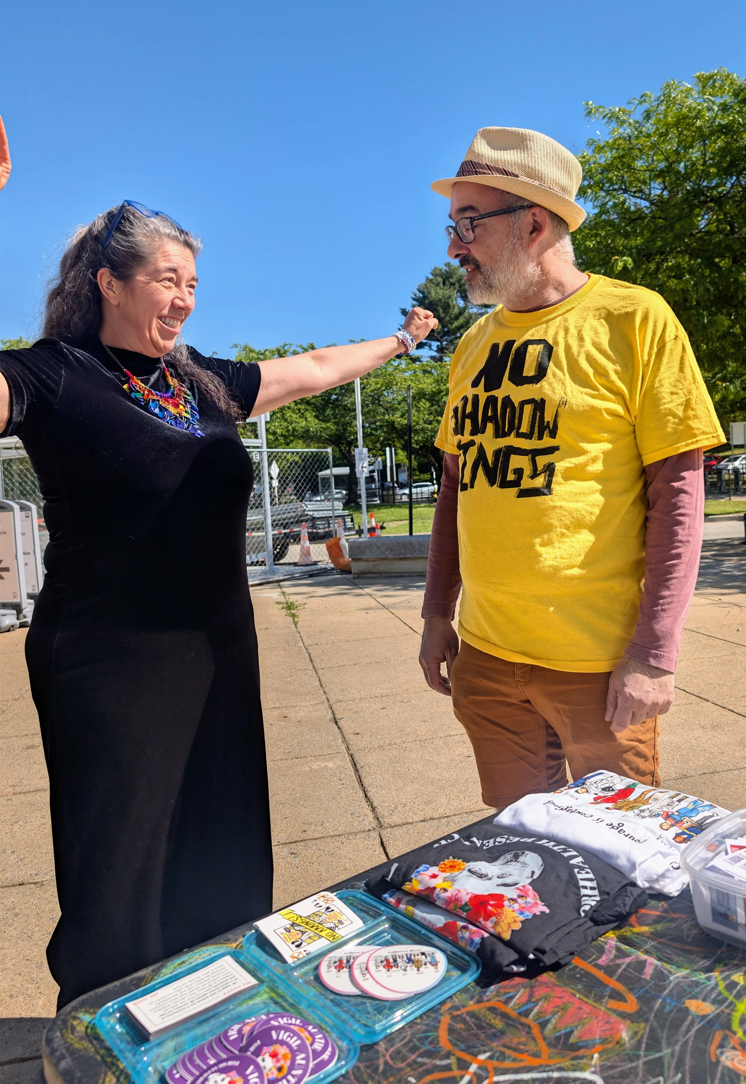 A woman raises her arms in triumph while smiling at a man in a No Shadow Kings shirt