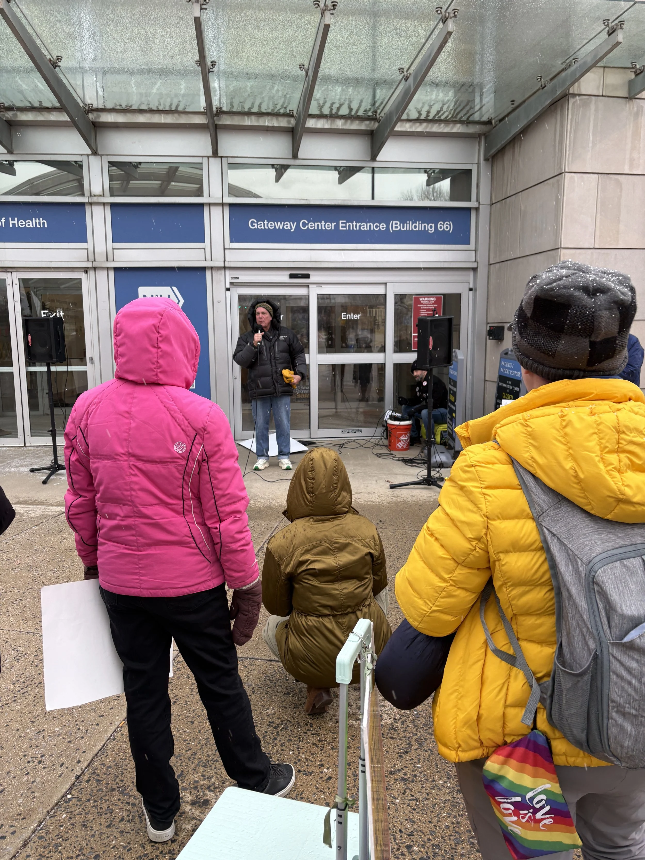 A small crowd listens to the speaker at an NIH vigil
