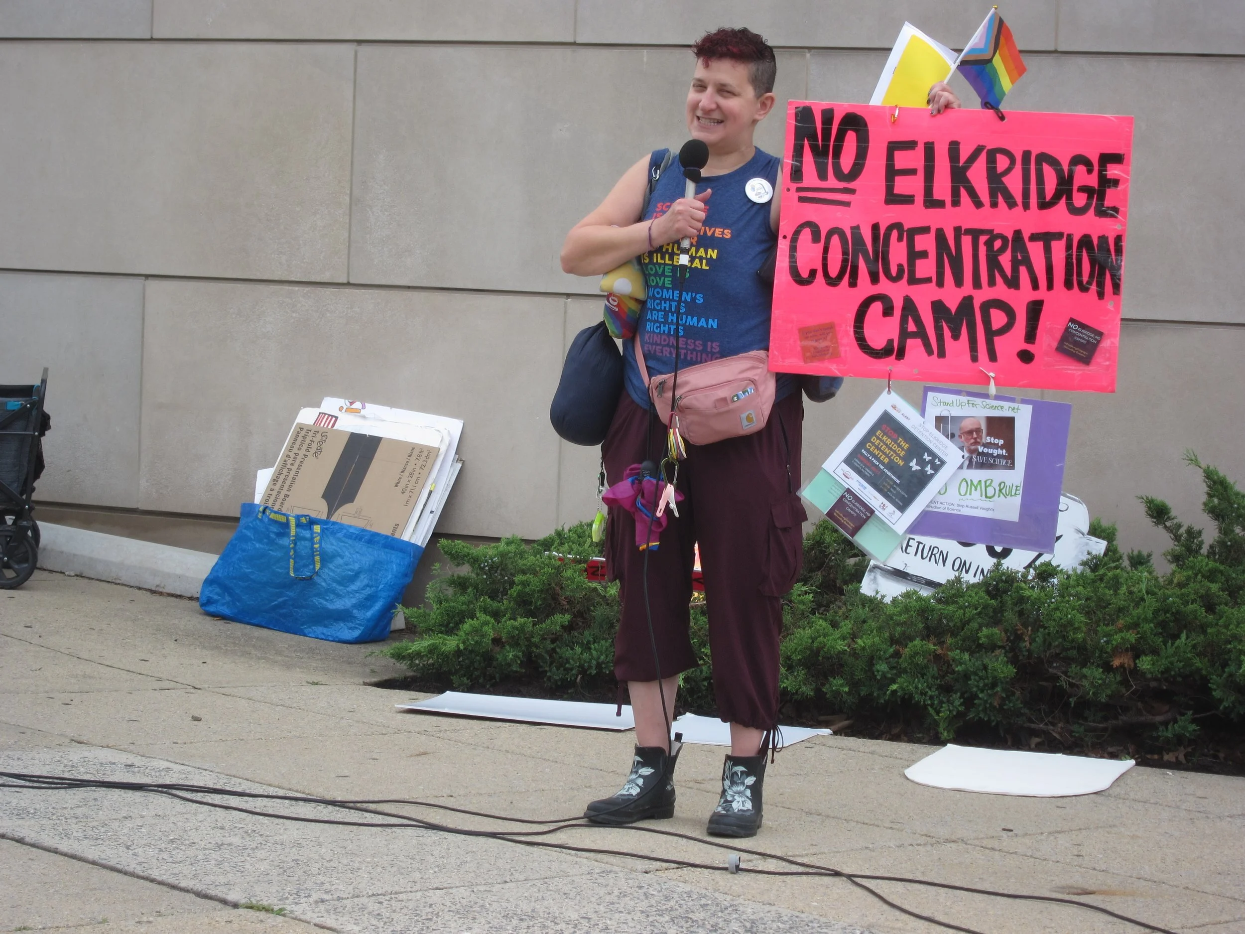A person speaks into a microphone while holding a protest sign