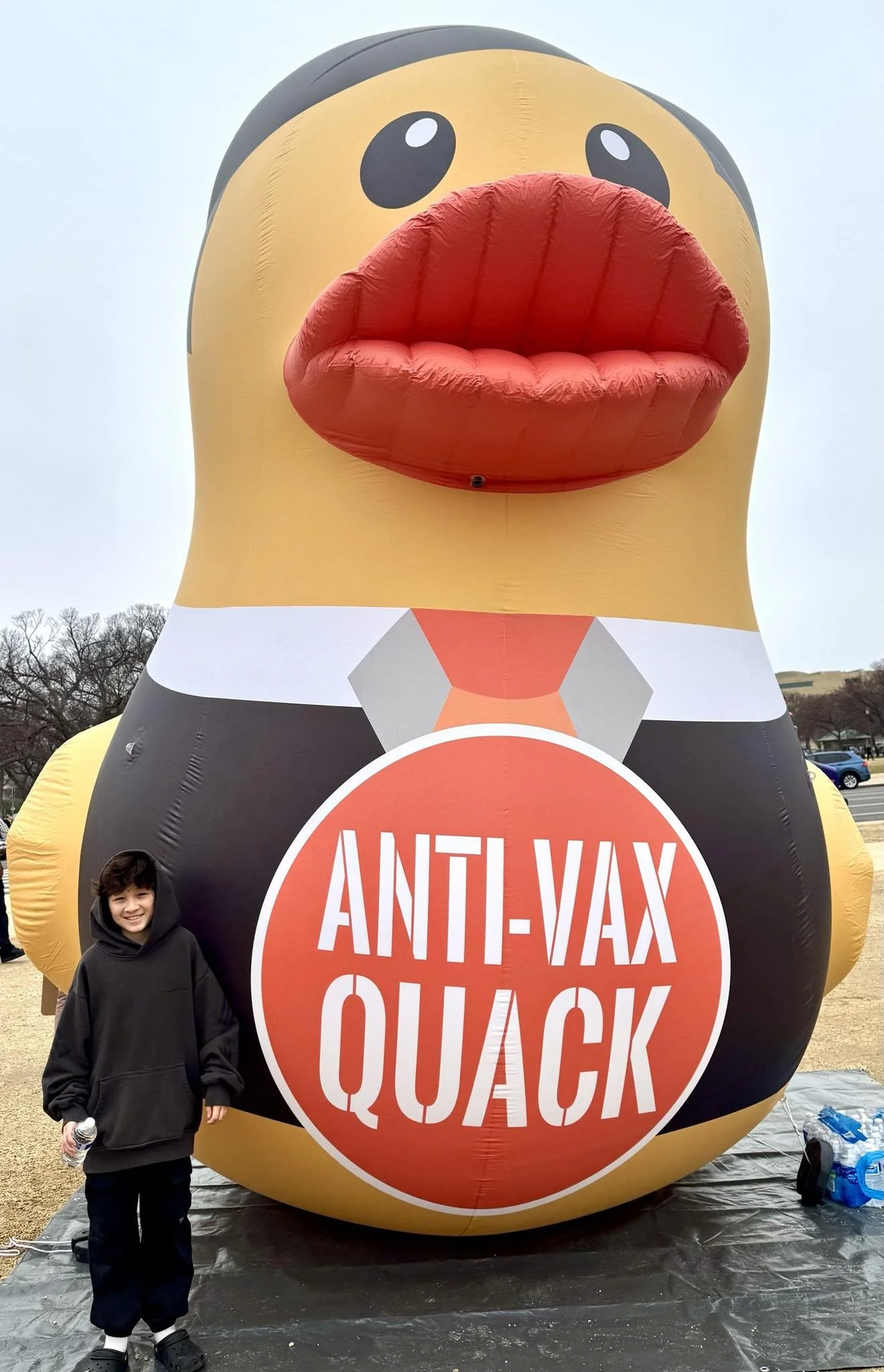 A child with a large inflatable duck saying "Anti-Vax Quack."