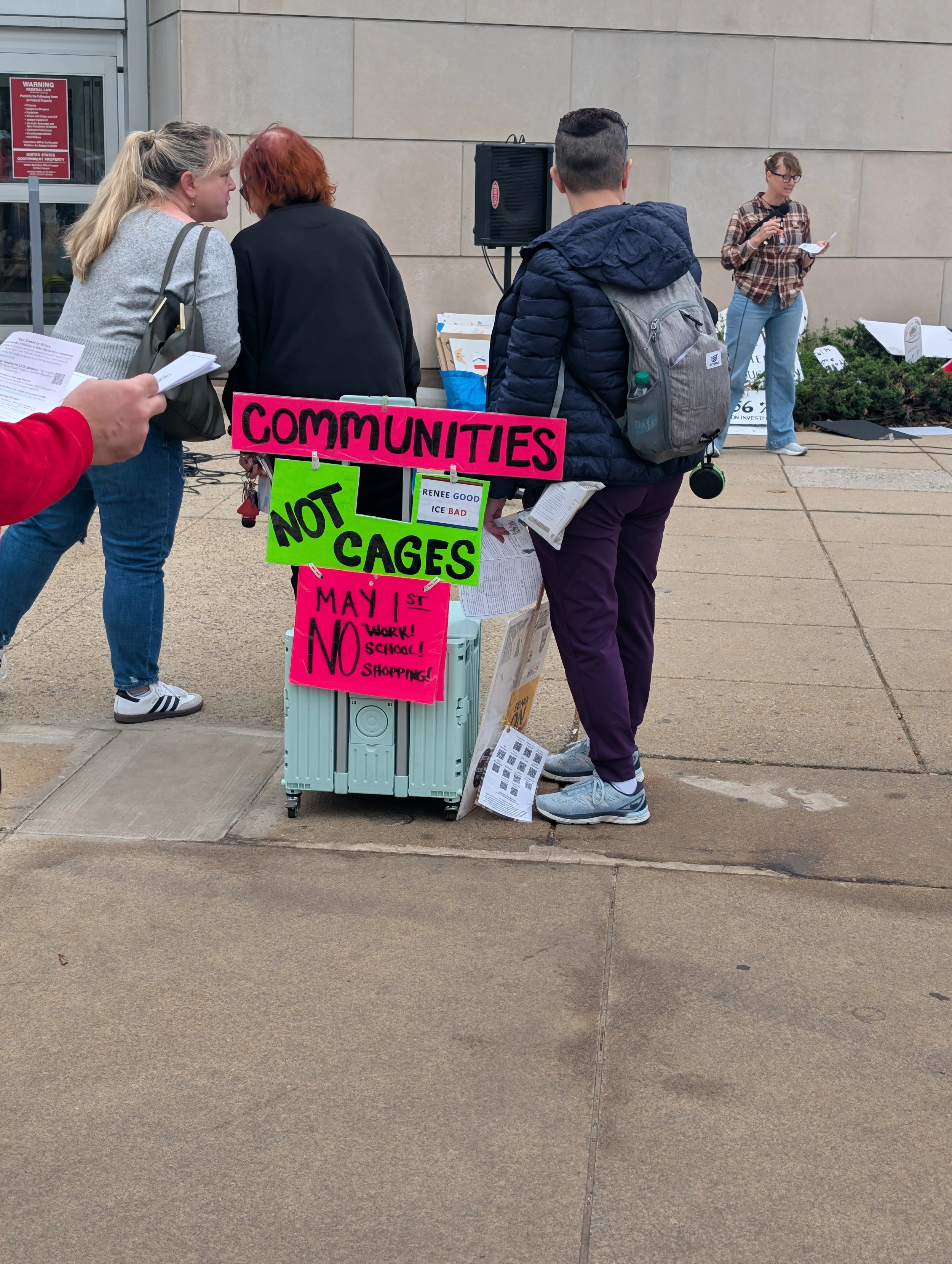 people watching the speaker at the NIH vigil, with a  protest sign saying "Communities not cages"