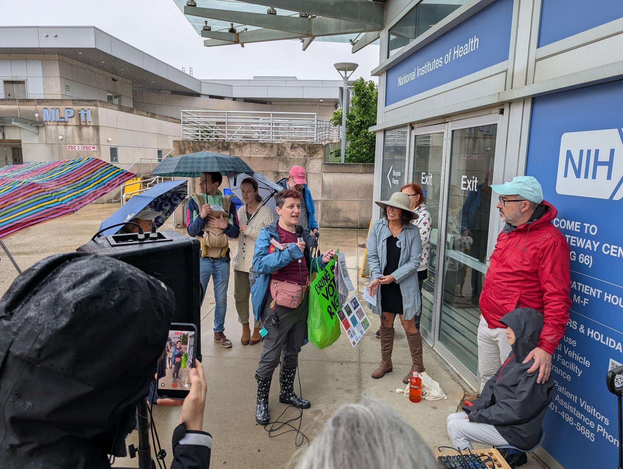 Woman with green bag and rain boots speaks into a microphone to attendees