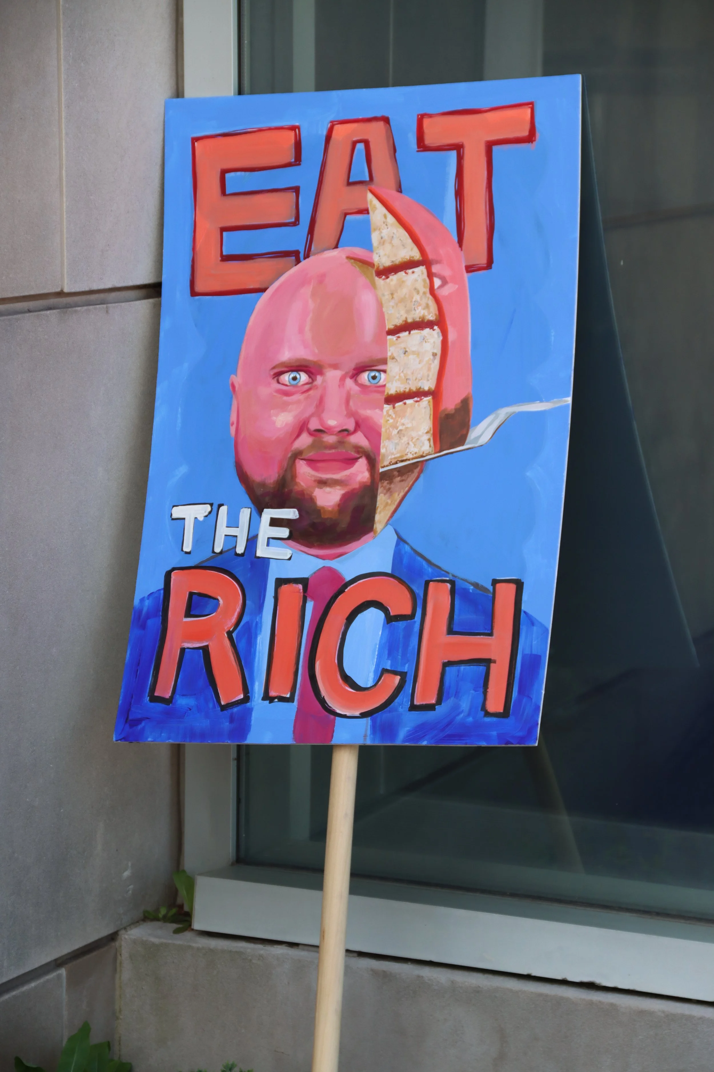 A protest sign saying "eat the rich' and showing JD Vance as cake