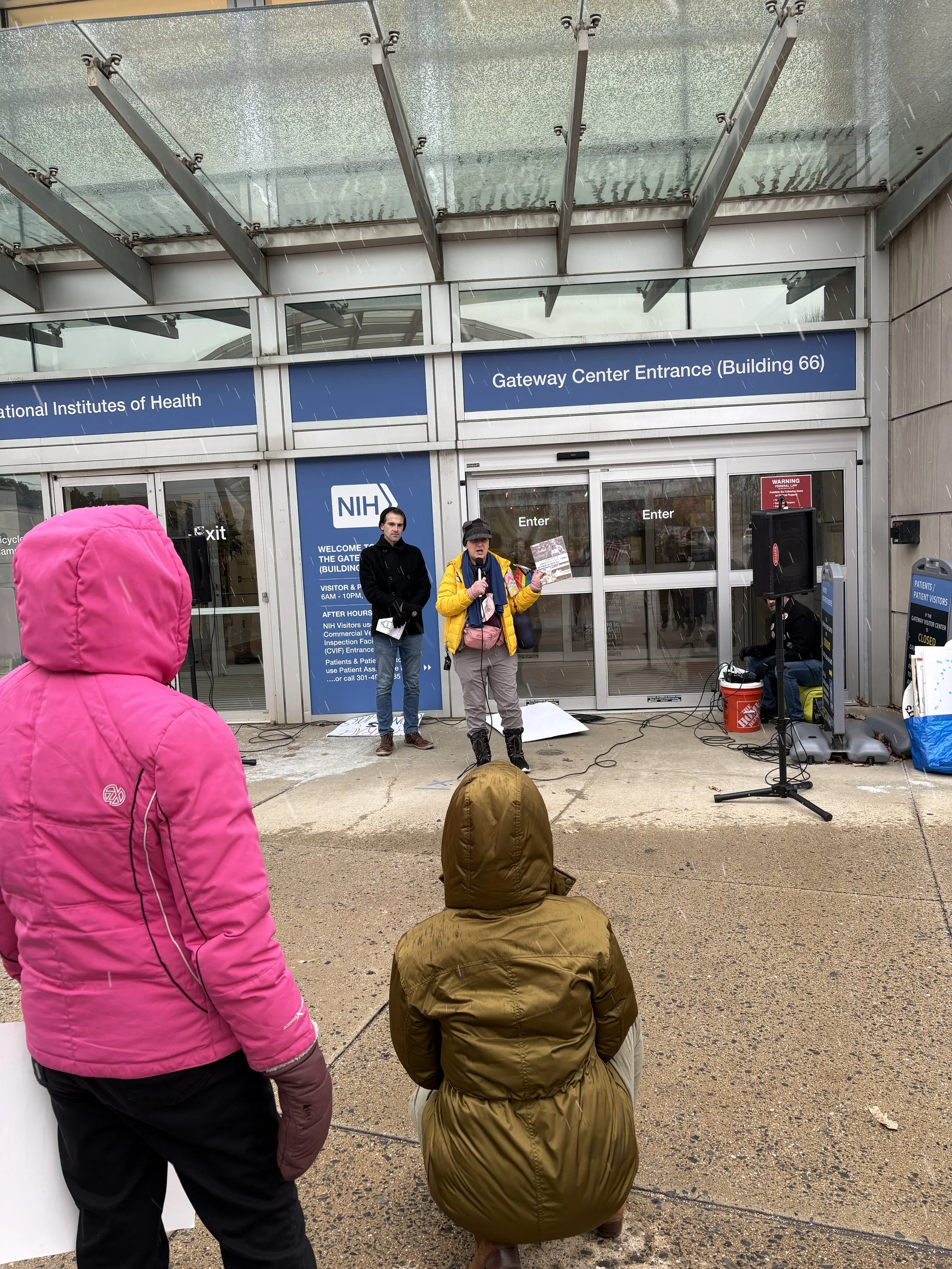 People listen to the person speaking at an NIH vigil
