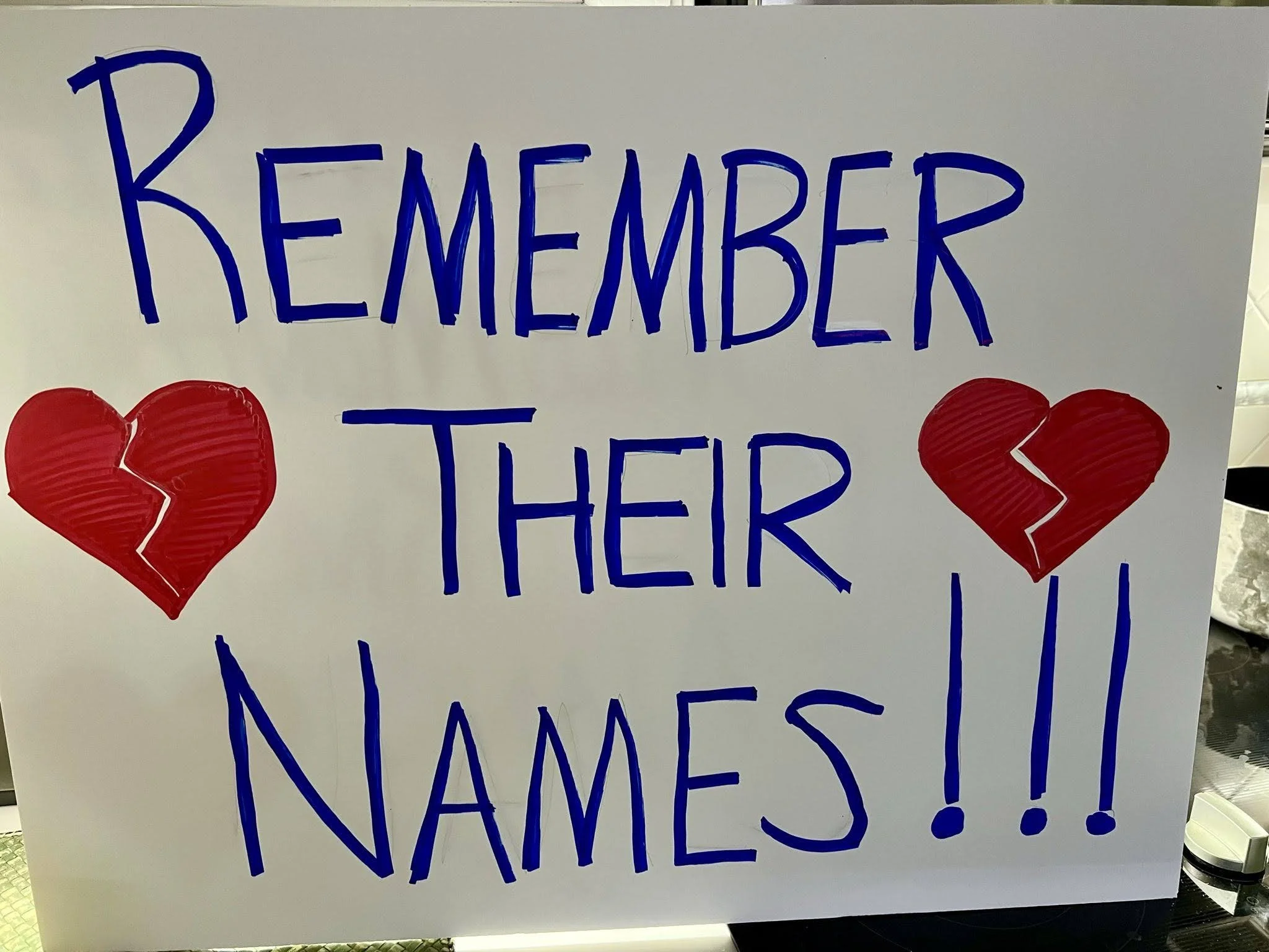A protest signs showing broken heart icons and saying "remember their names"