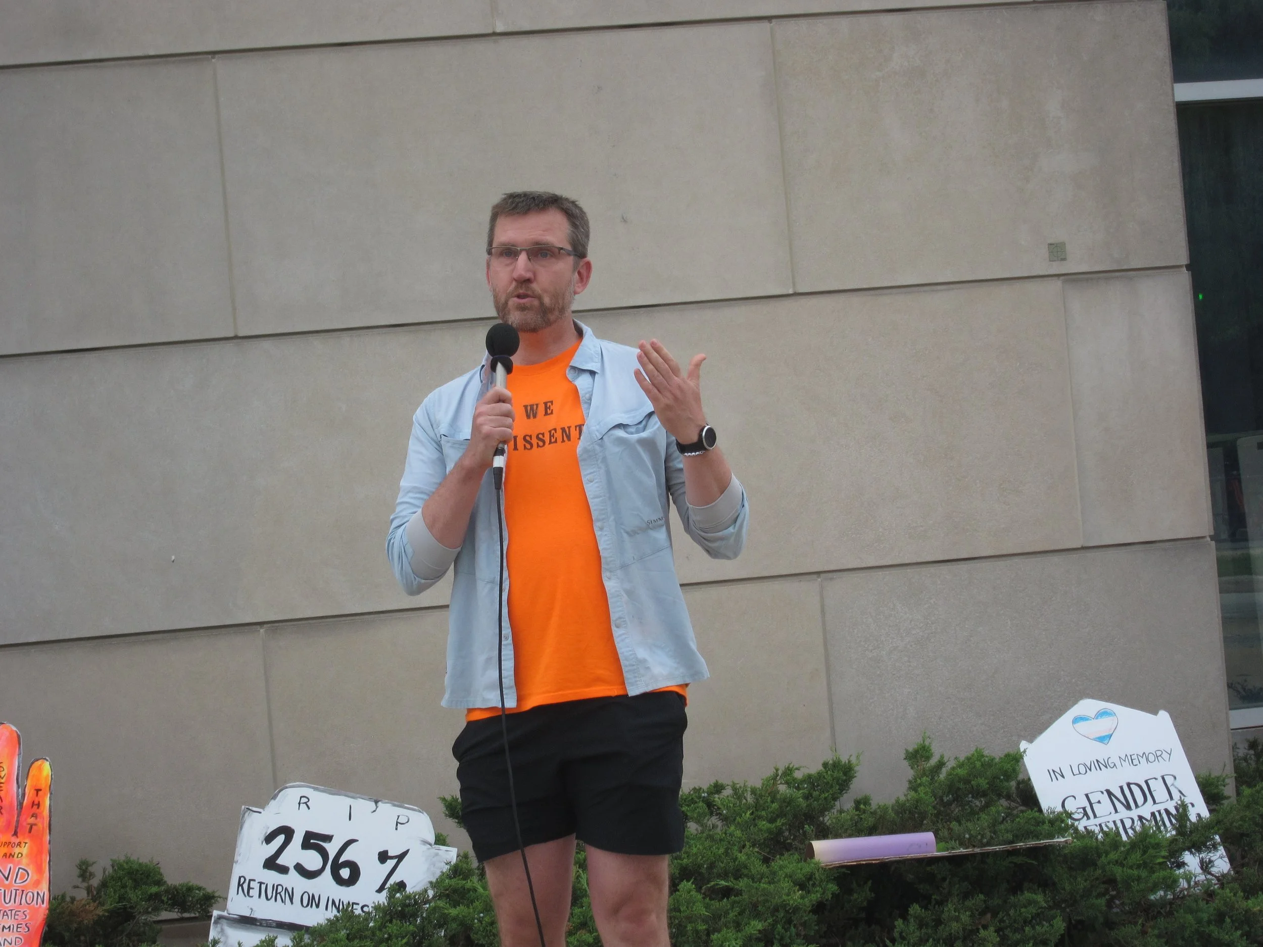 A man wearing a  "We Dissent" shirt speaks into a microphone