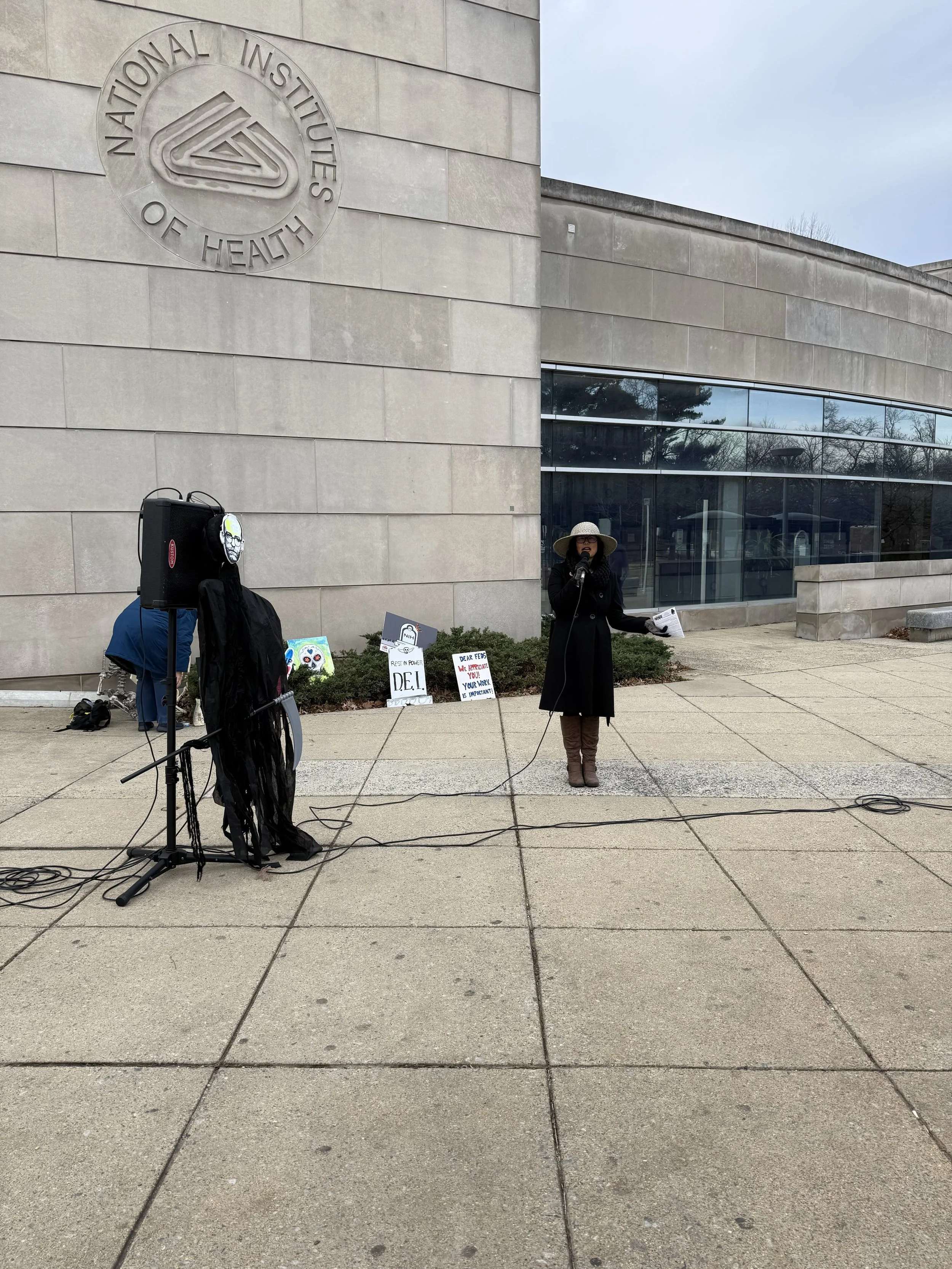 A person speaks into a microphone at an NIH vigil