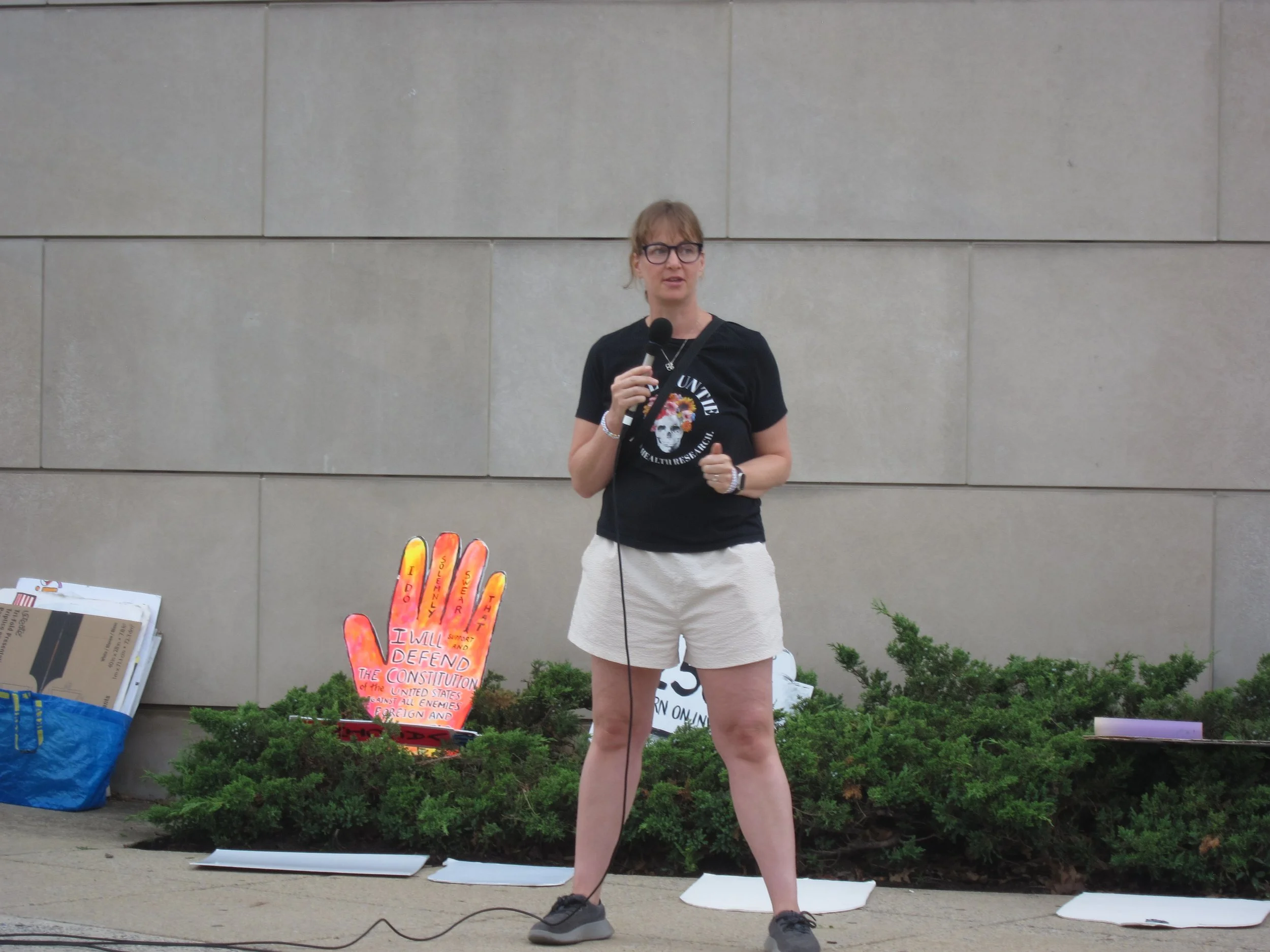 A woman wearing a Vigil Auntie shirt speaks into a microphone