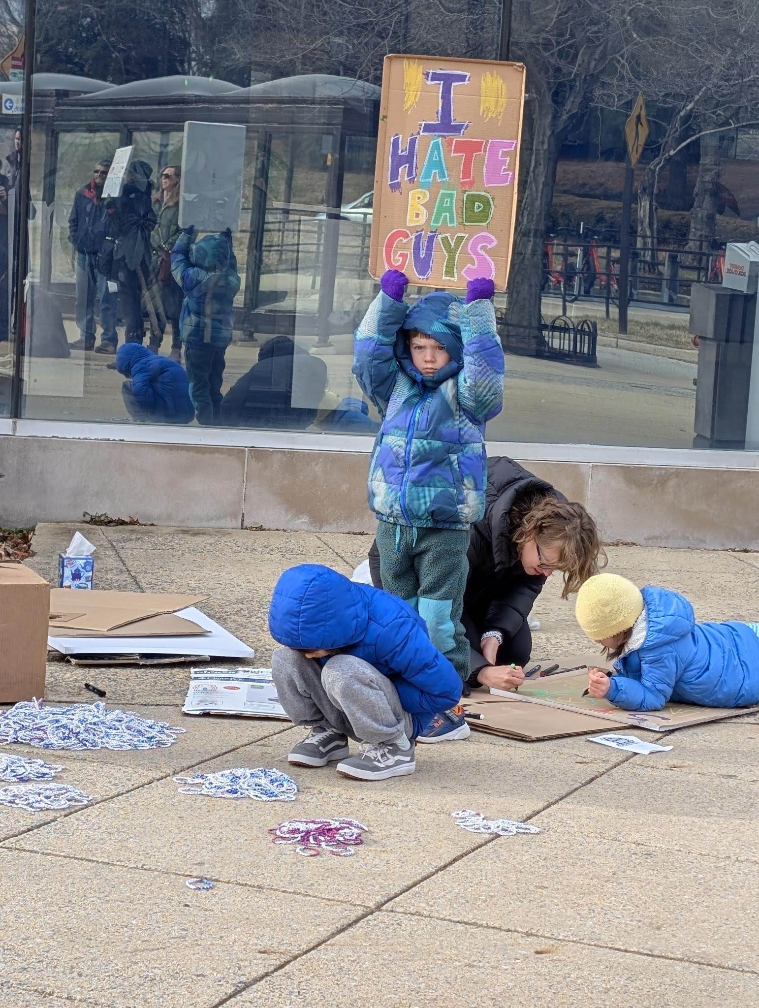 Children make protest signs, one reading "I hate bad guys," at an NIH vigil