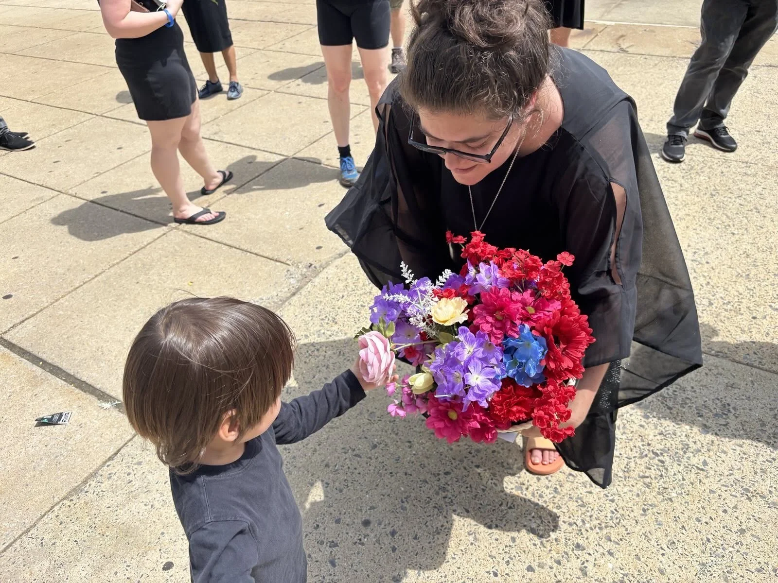 A little boy takes a flower from a bouquet held by a woman