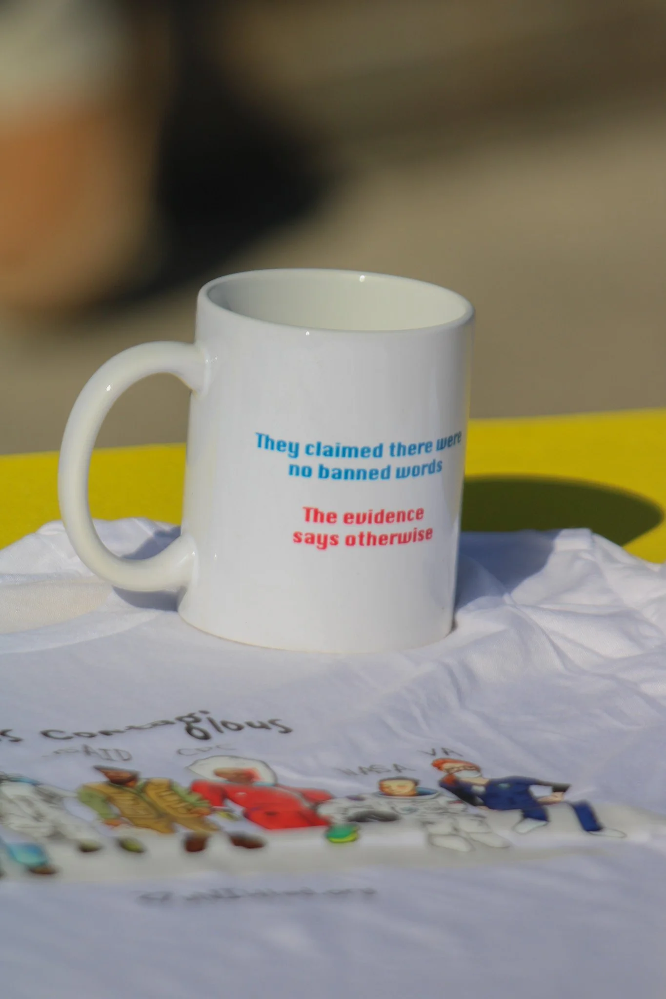 A coffee mug and a T-shirt on a merch table