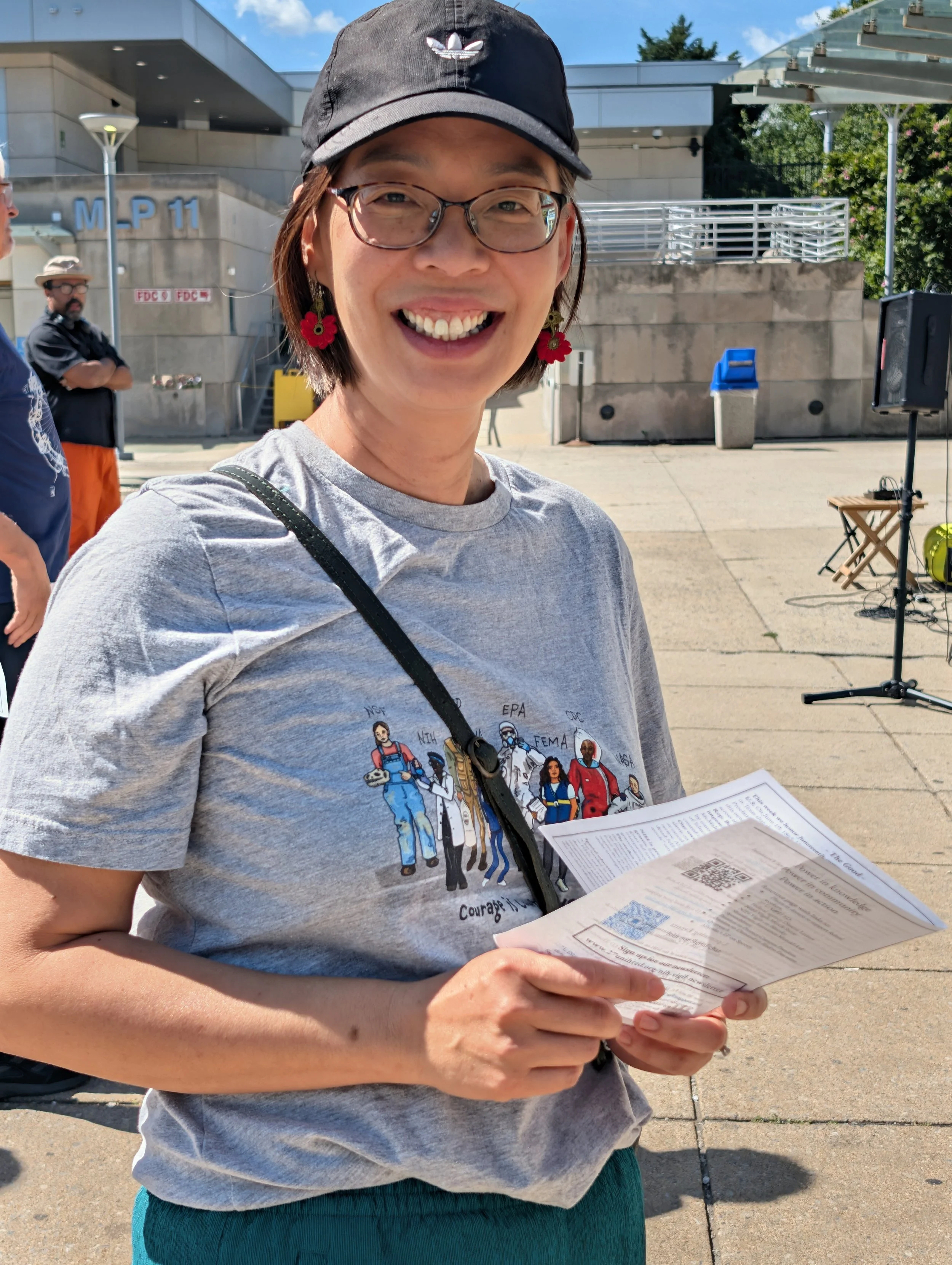 A smiling Sylvia Chou holds printed handouts outside an NIH campus entrance.