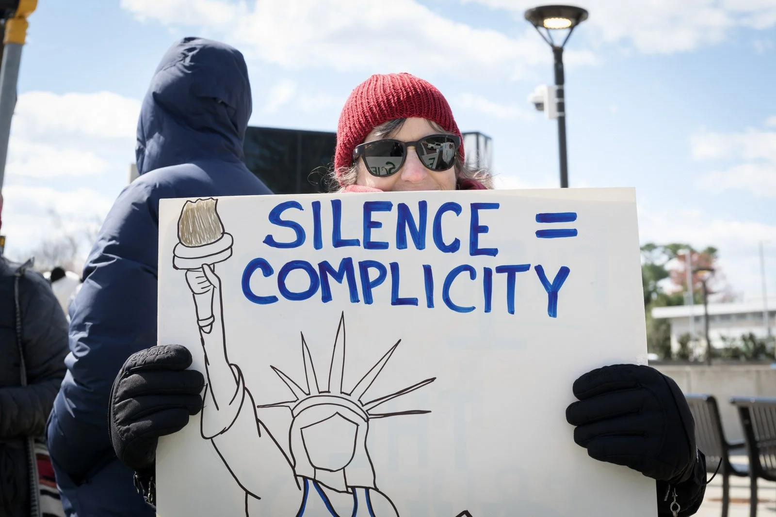 A protestor holding a sign saying "Silence equals complicity"