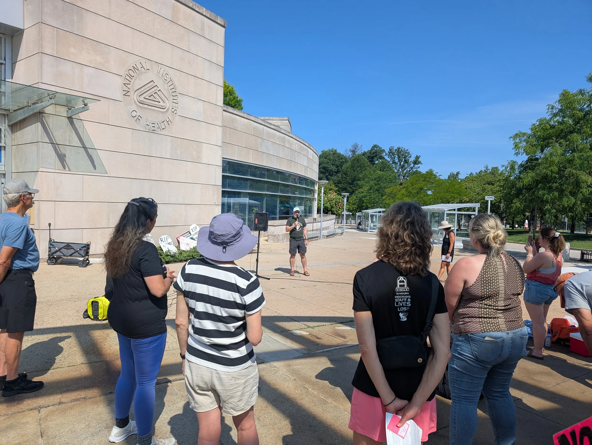NIH Vigil attendees listen as a speaker addresses the group outside the NIH Gateway Center.