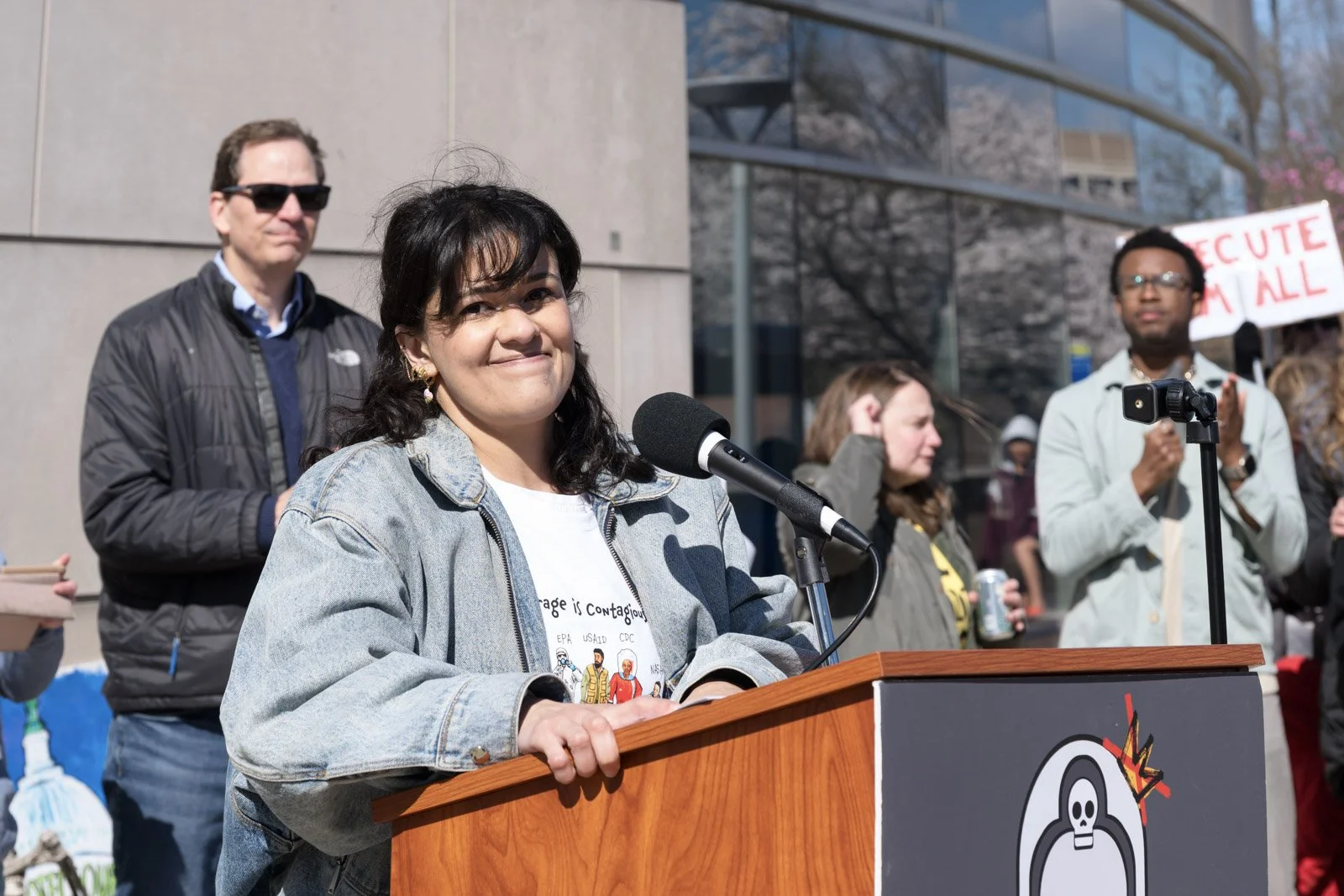 A woman smiles at the camera while standing at the lectern to speak