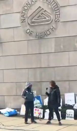 A person speaks to another speaker at an NIH vigil