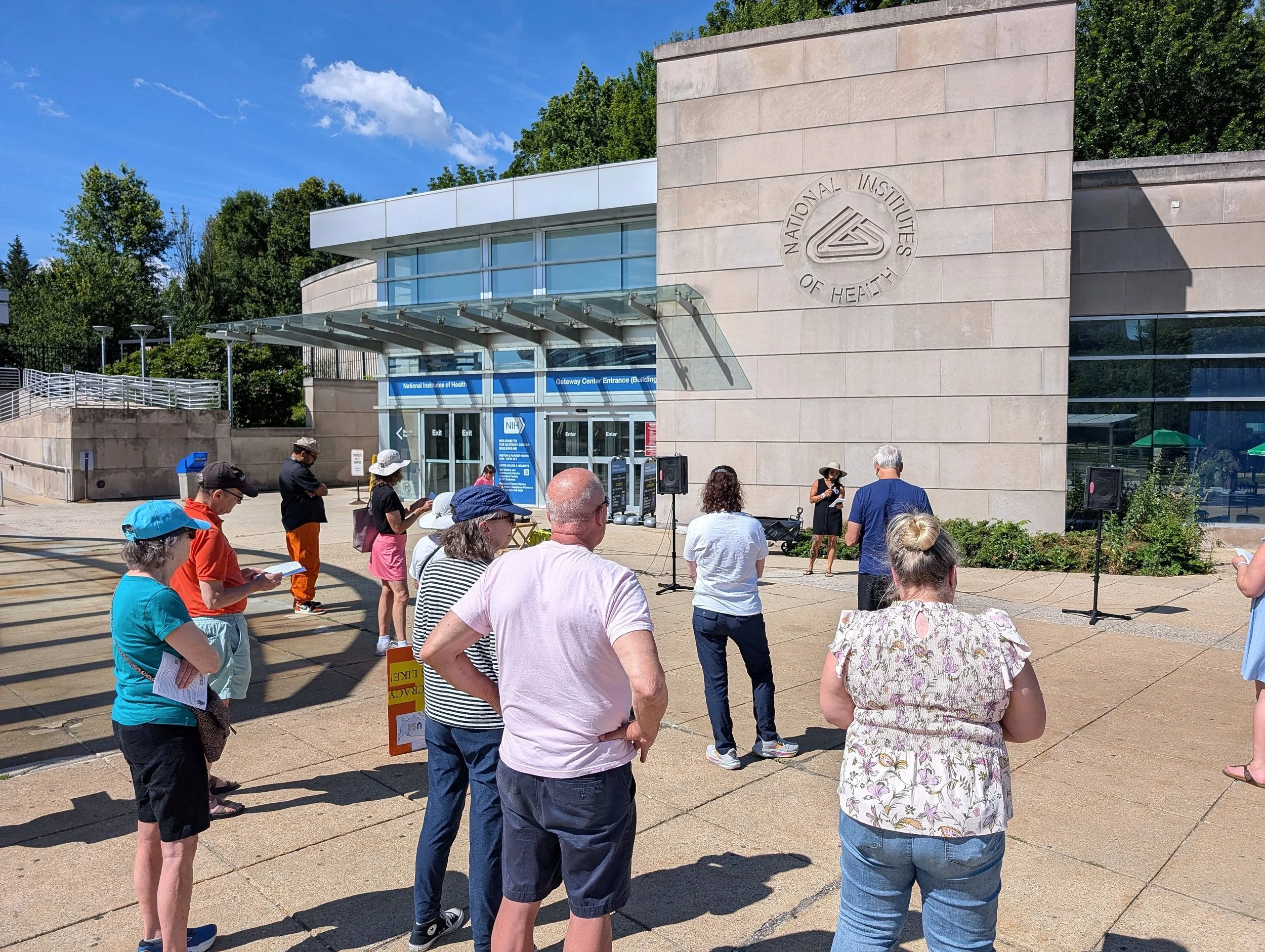 NIH Vigil attendees listen to a speaker outside the NIH Gateway Center entrance.