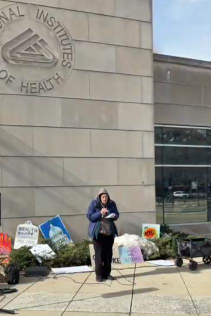 A person speaks at an NIH vigil