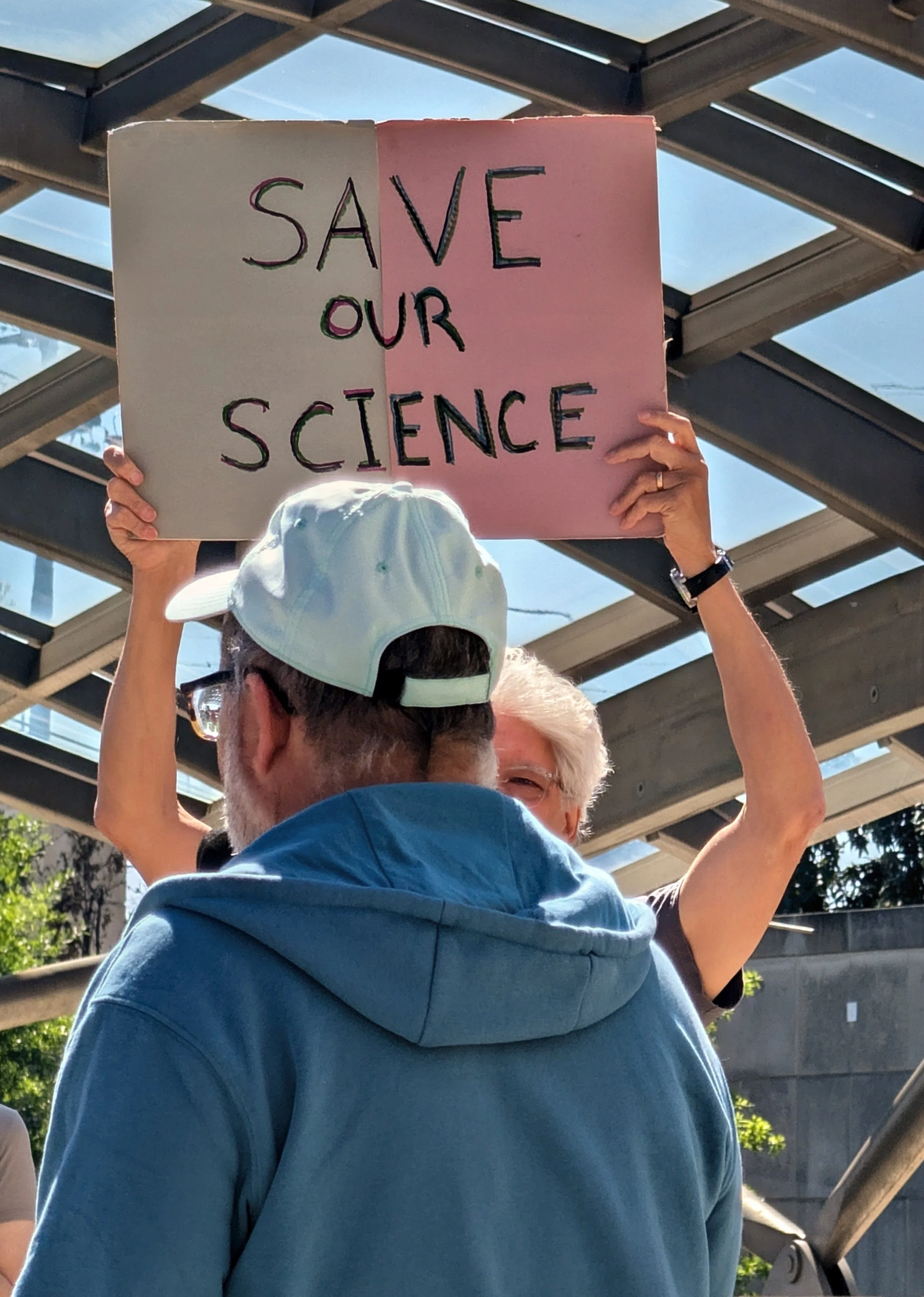 A vigil attendees holds up a "Save Our Science" protest sign with the vigil speaker facing them
