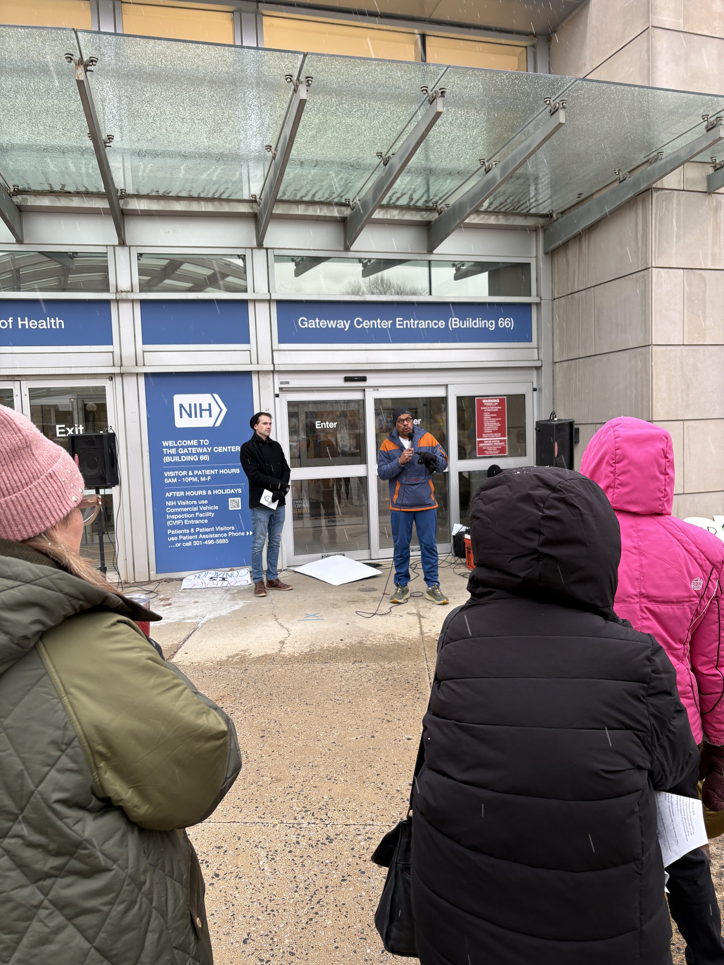 People watch a person speaking at the NIH vigil
