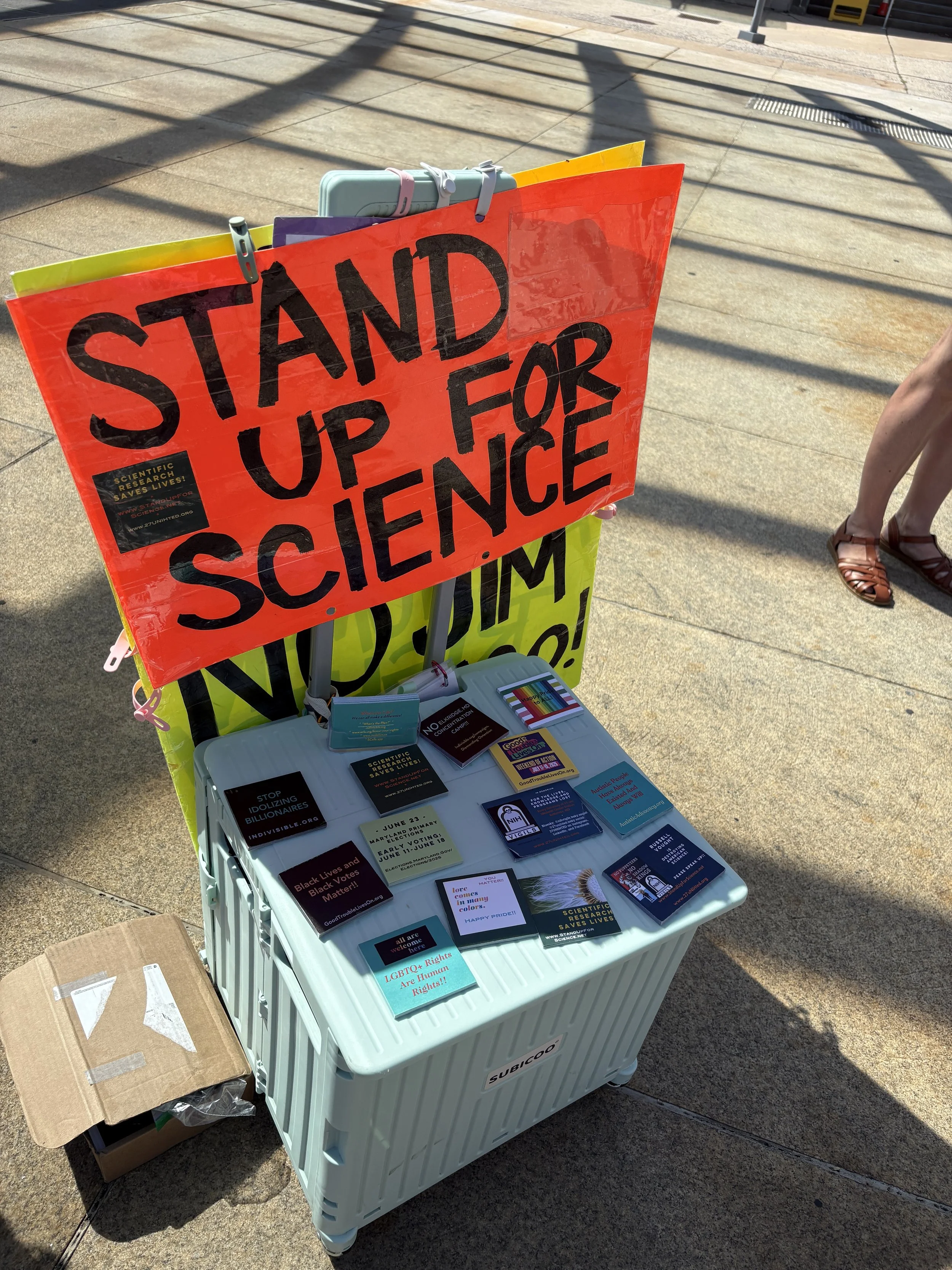 A “Stand Up for Science” sign and informational handouts sit on a rolling supply bin .