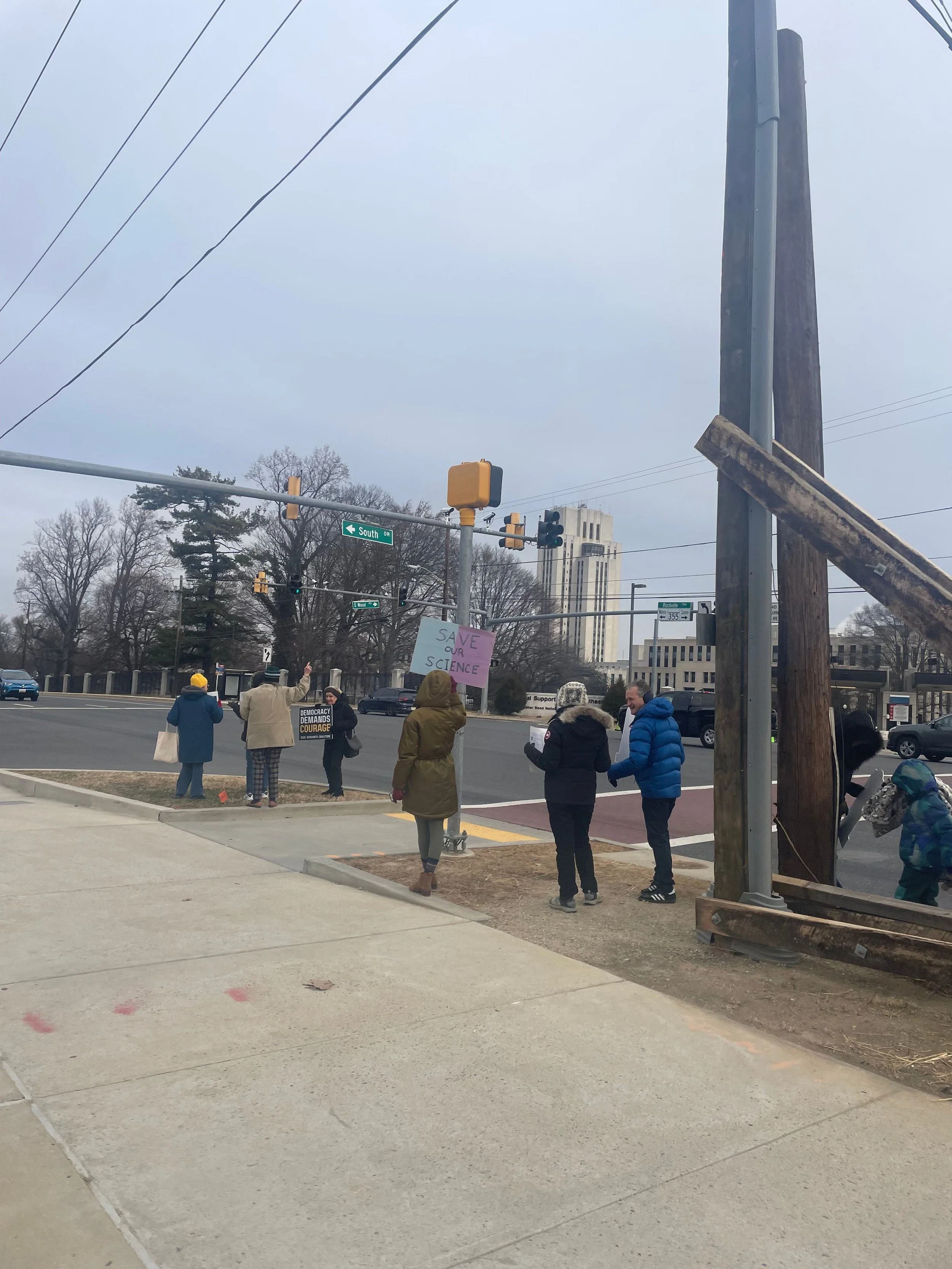 Protesters hold signs along the roadside after an NIH vigil