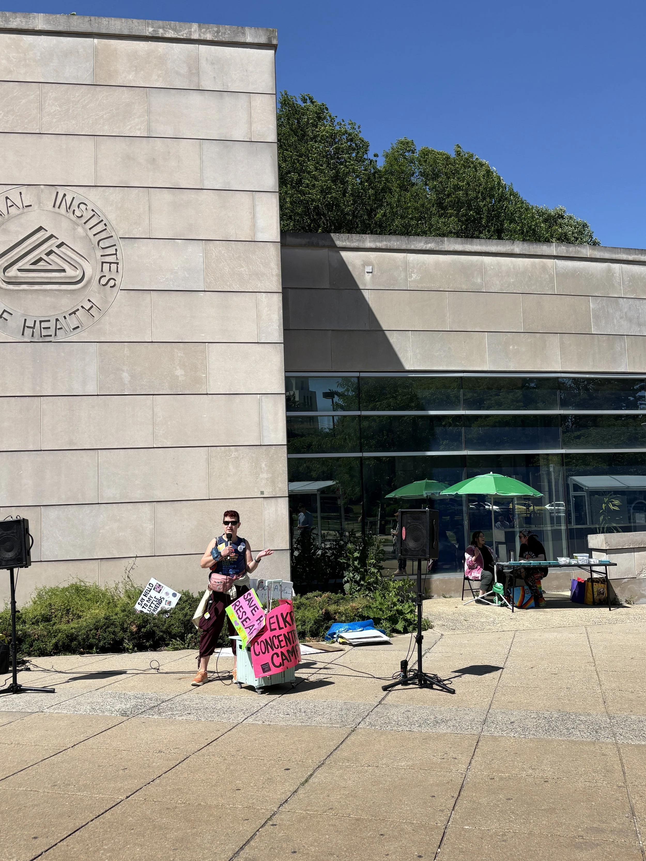 A speaker at the vigil with the merch table in the background