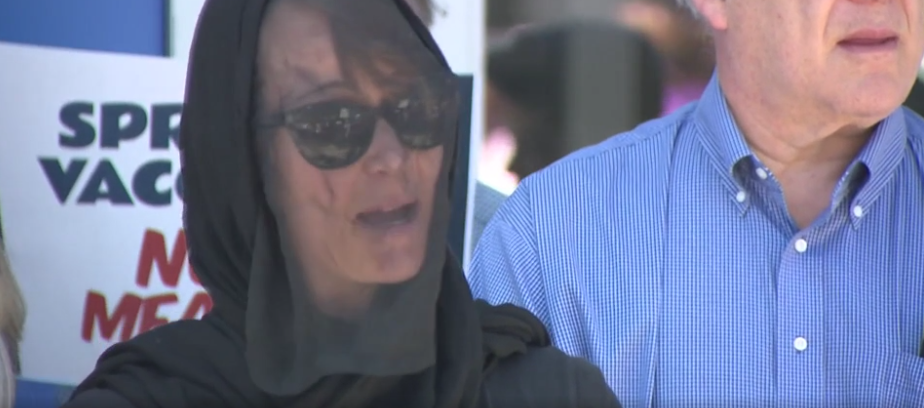 A woman in black mourning attire speaks at the vigil