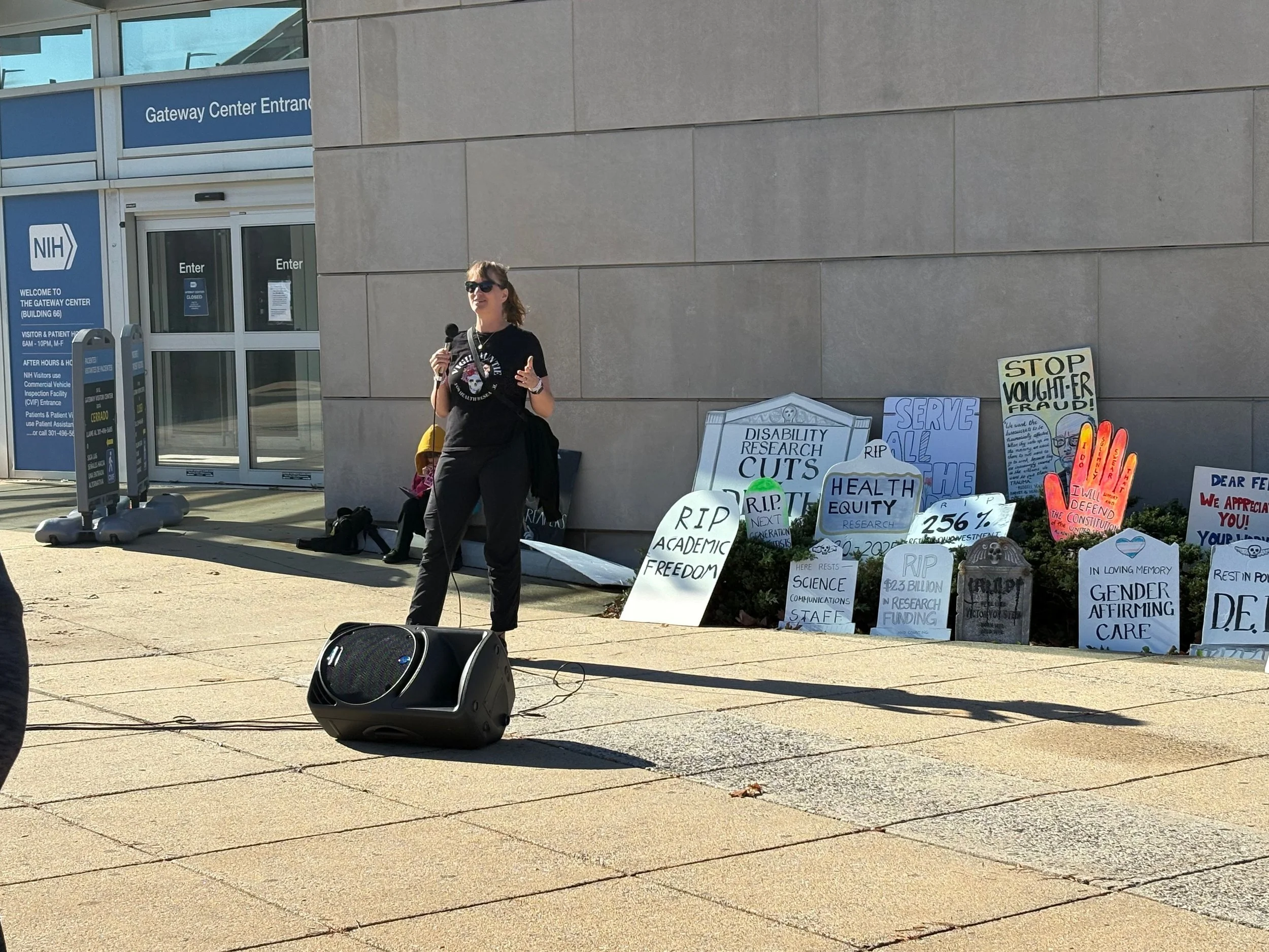 A woman speaks into a microphone at an NIH vigil