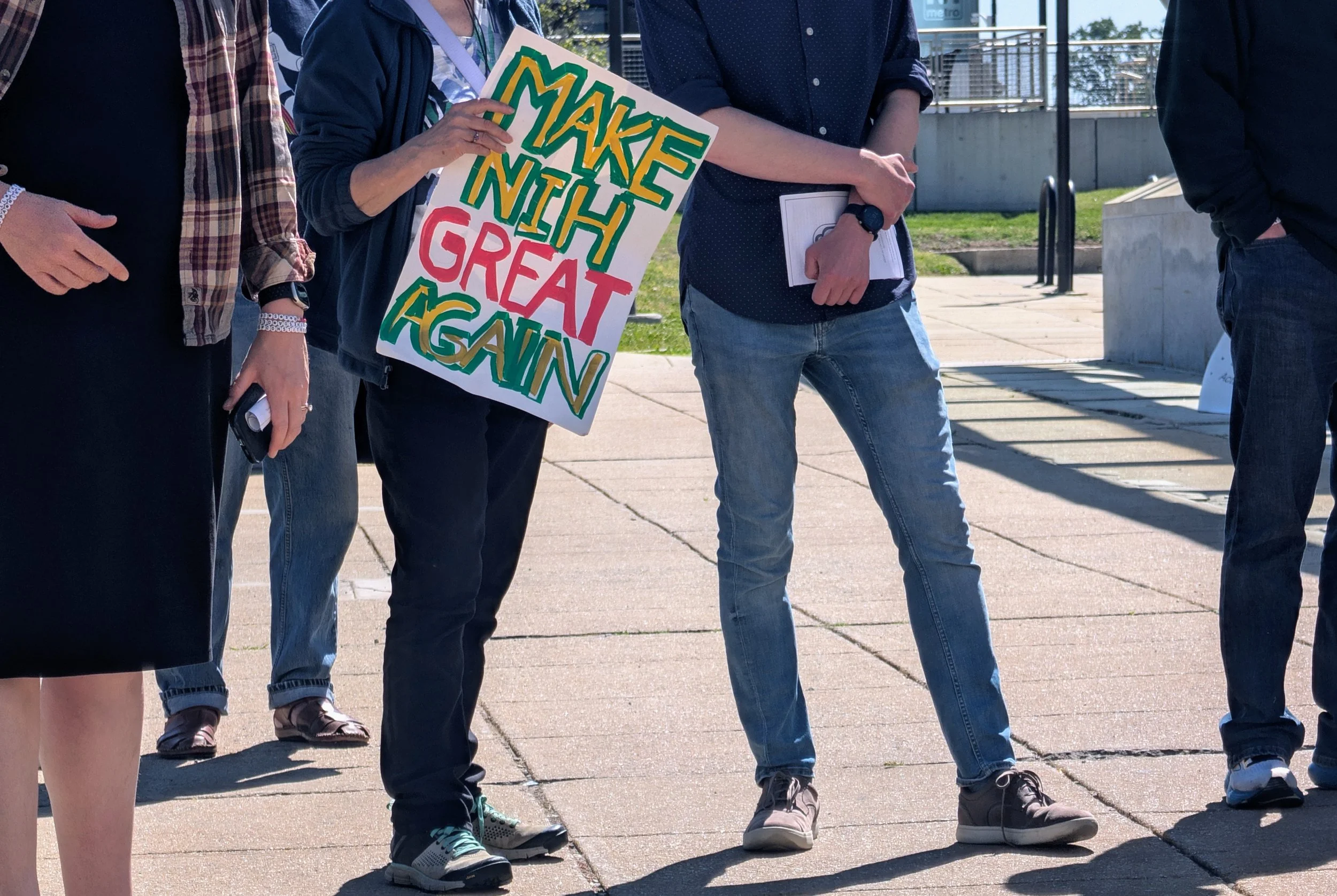 Someone in the crowd of vigil spectators holds a sign that says "Make NIH Great Again"