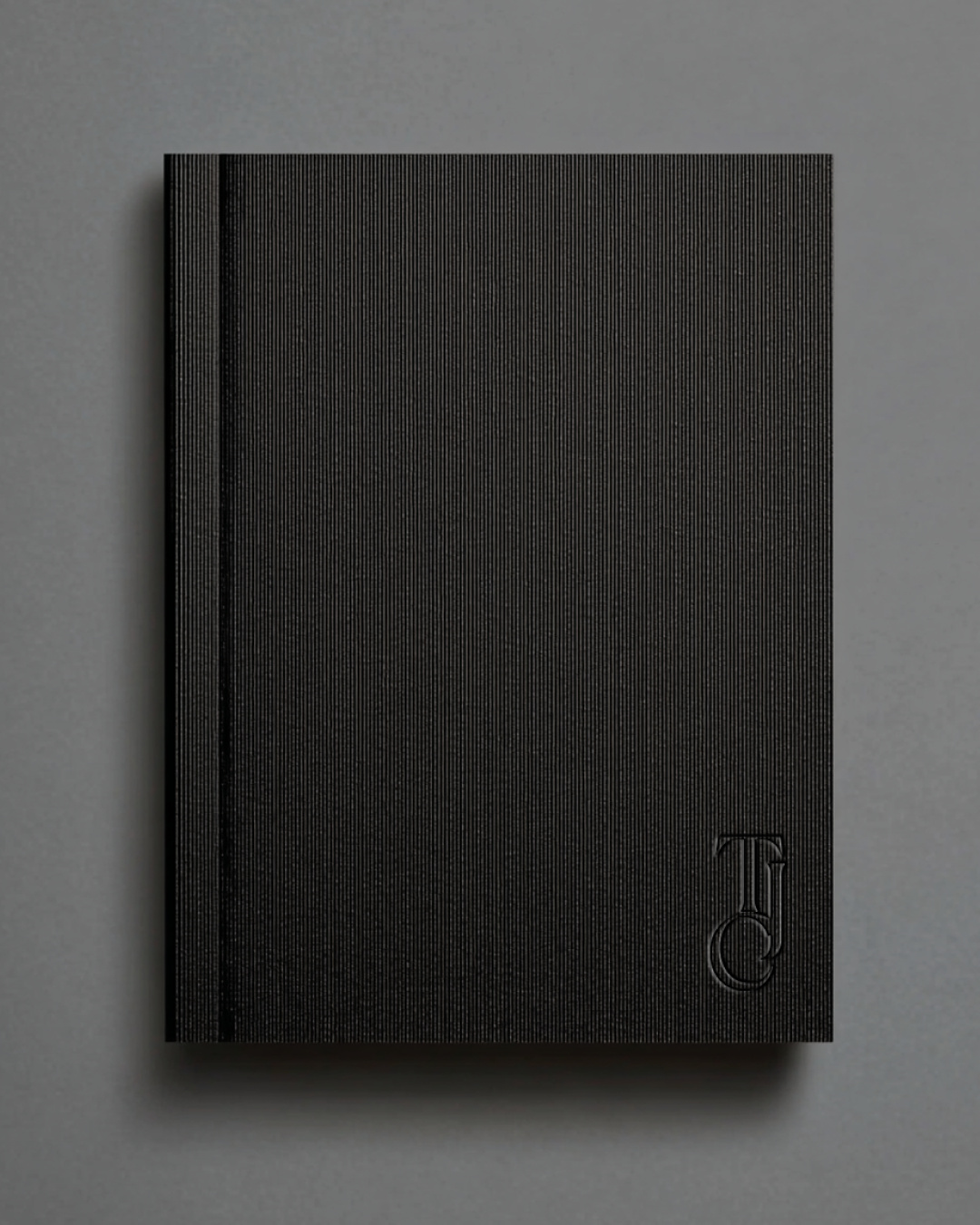 Black textured notebook with a monogram embossed in the bottom right corner, placed on a gray surface.