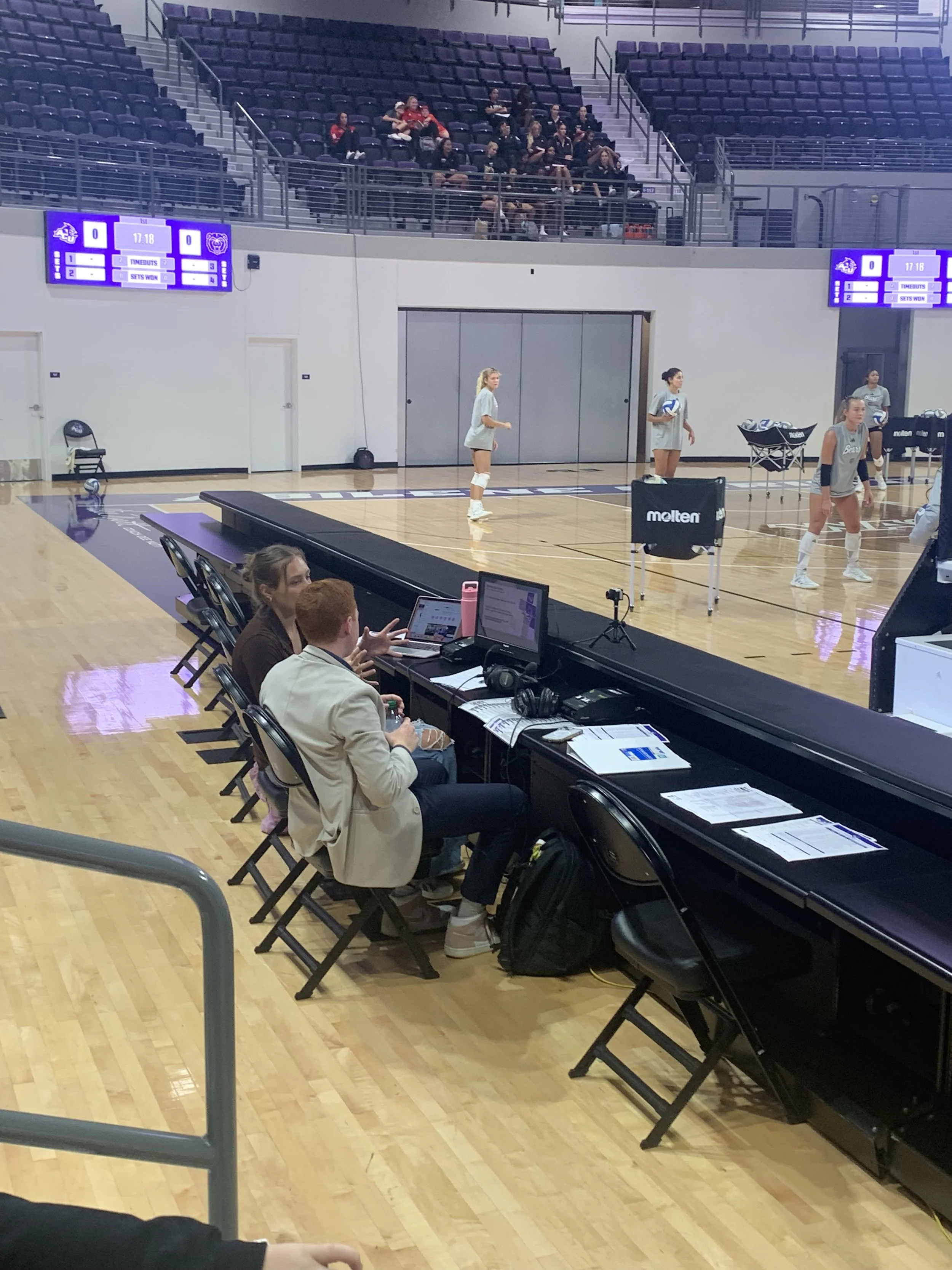 A modern building with wooden and white exterior, large glass window, situated in a grassy field with mountains in the background.