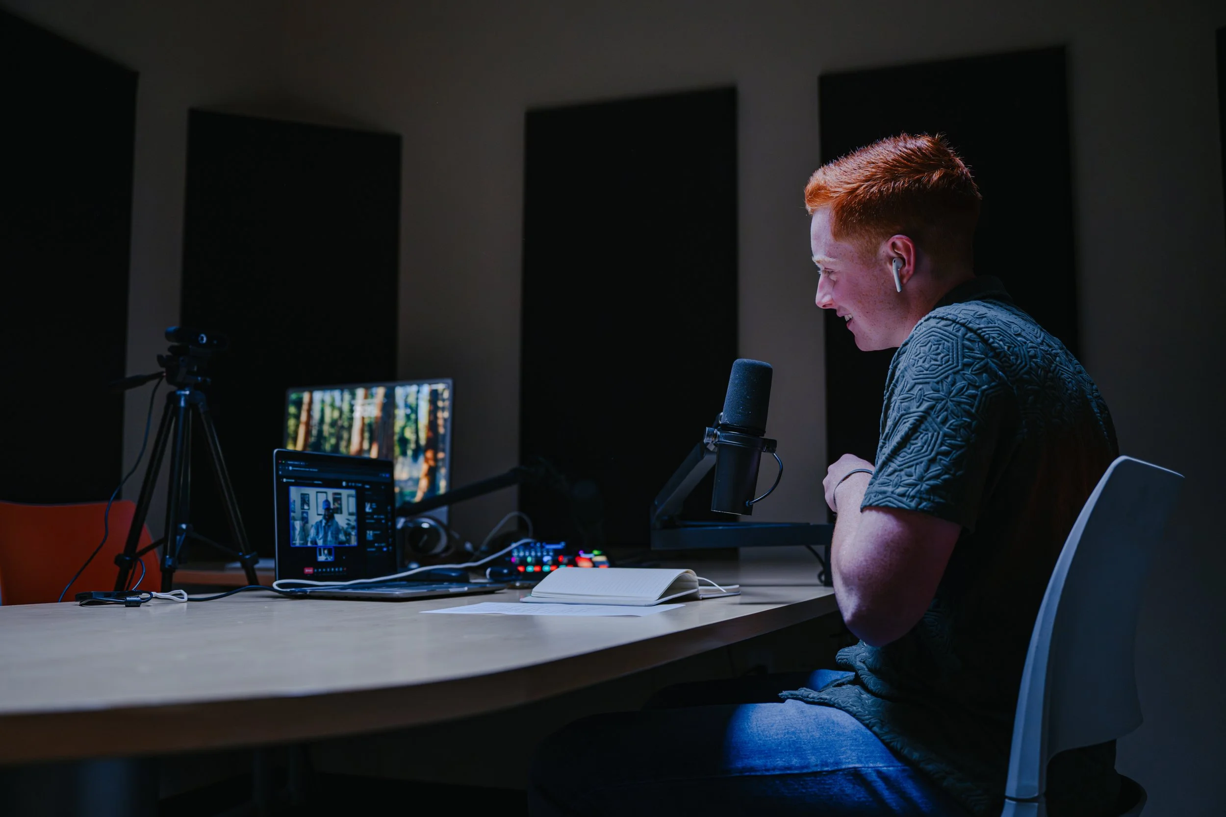 A mountain landscape with snow-capped peaks in the background and rolling hills with green and brown vegetation in the foreground. There is a modern building on one of the hills.